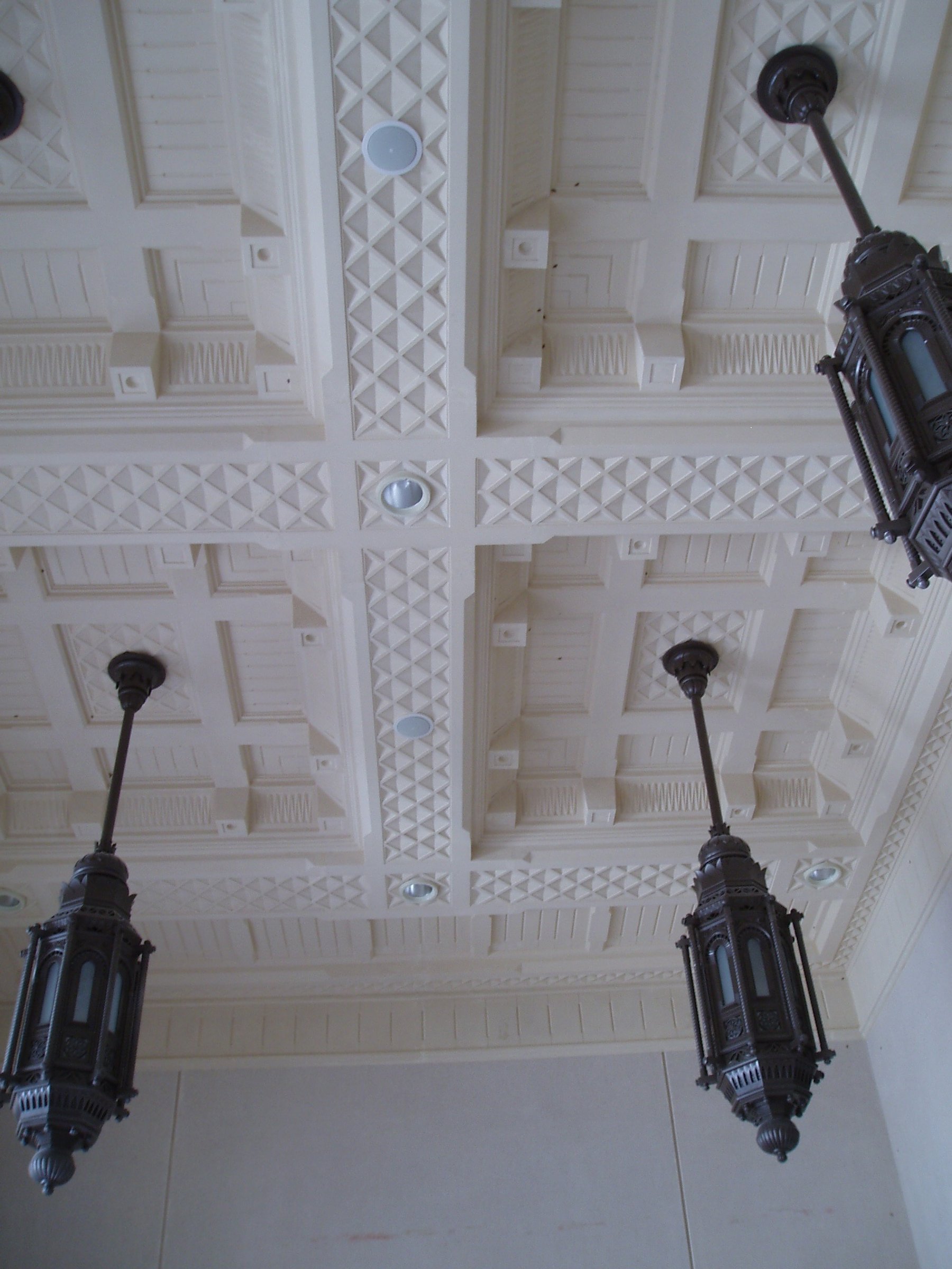 Coffered exterior ceiling with geometric relief and suspended architectural lanterns