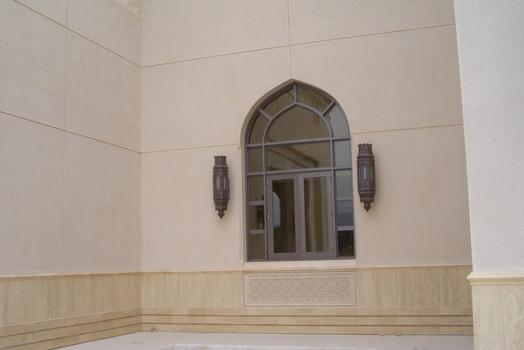 Pointed-arch exterior window framed by GRC detailing and wall-mounted lanterns