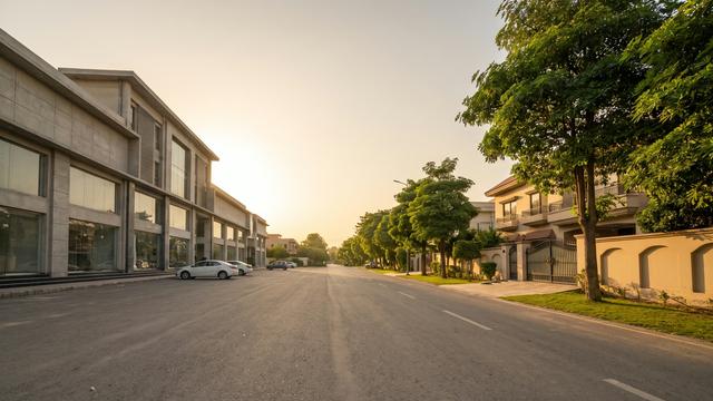 Split street view in a planned Lahore suburb showing a modern commercial plaza on one side and a quiet residential street on the other