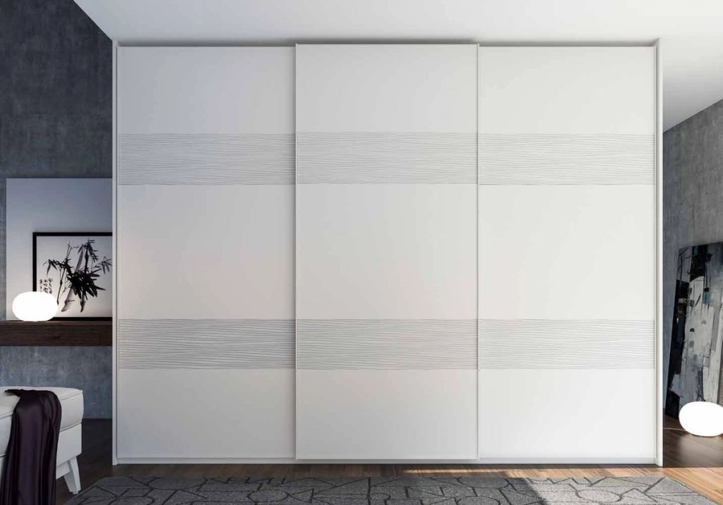 Puertas correderas de armario empotrado en tablero de una única pieza fresado especial y lacado blanco, en un dormitorio, composición tempro.