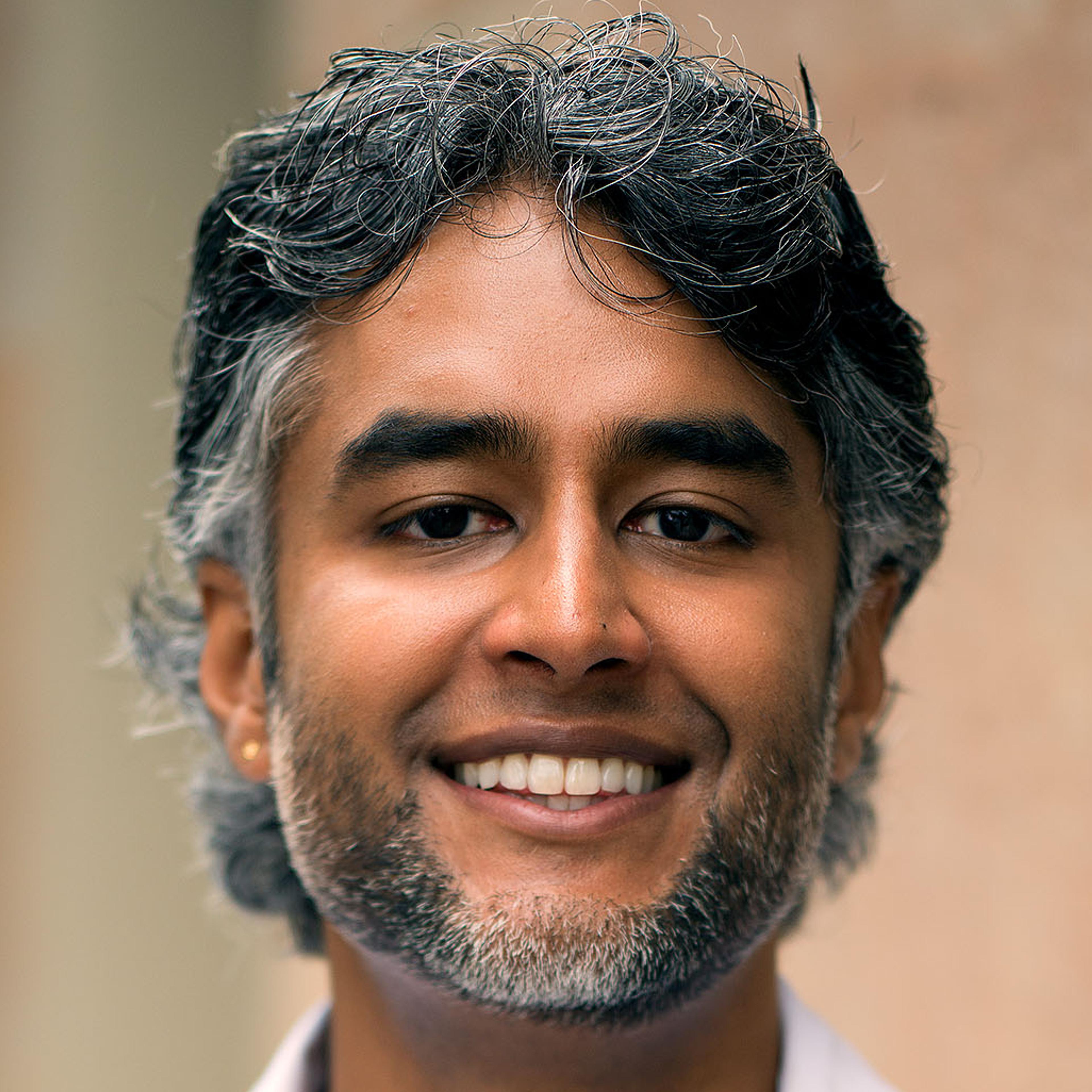 A headshot of a South Asian person with nice salt-and-pepper hair and a well-kept beard.