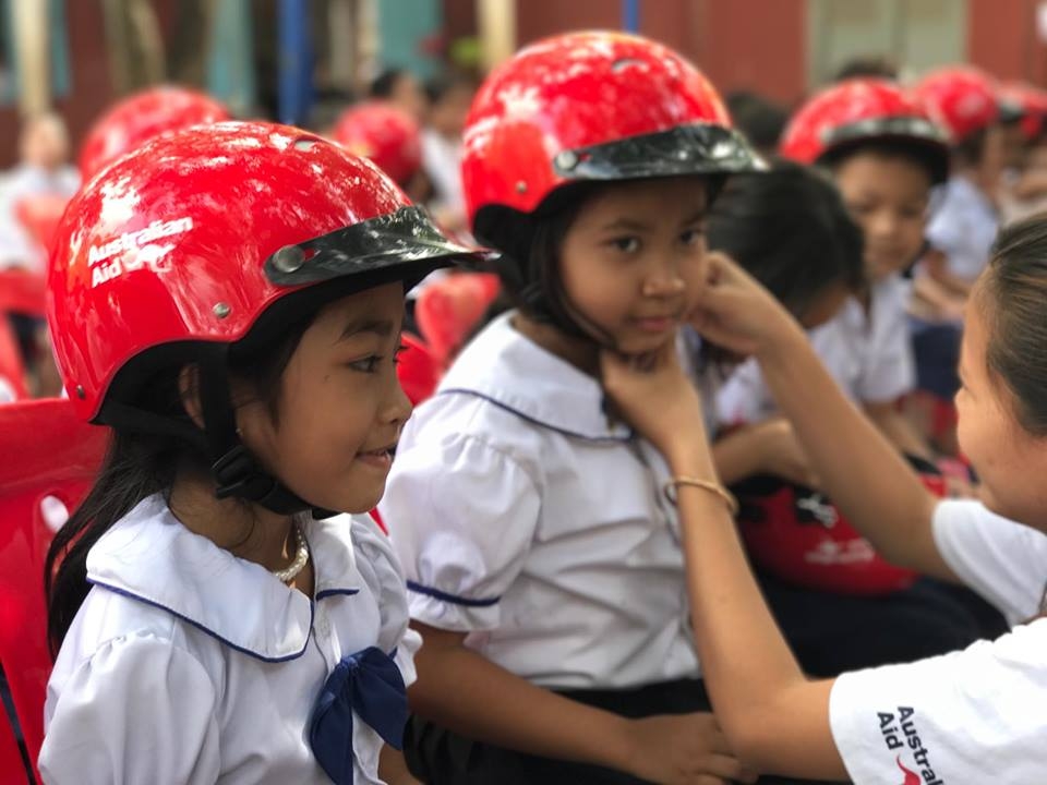 A YARS team member assists a Siem Reap primary school student on how to correctly wear her helmet.