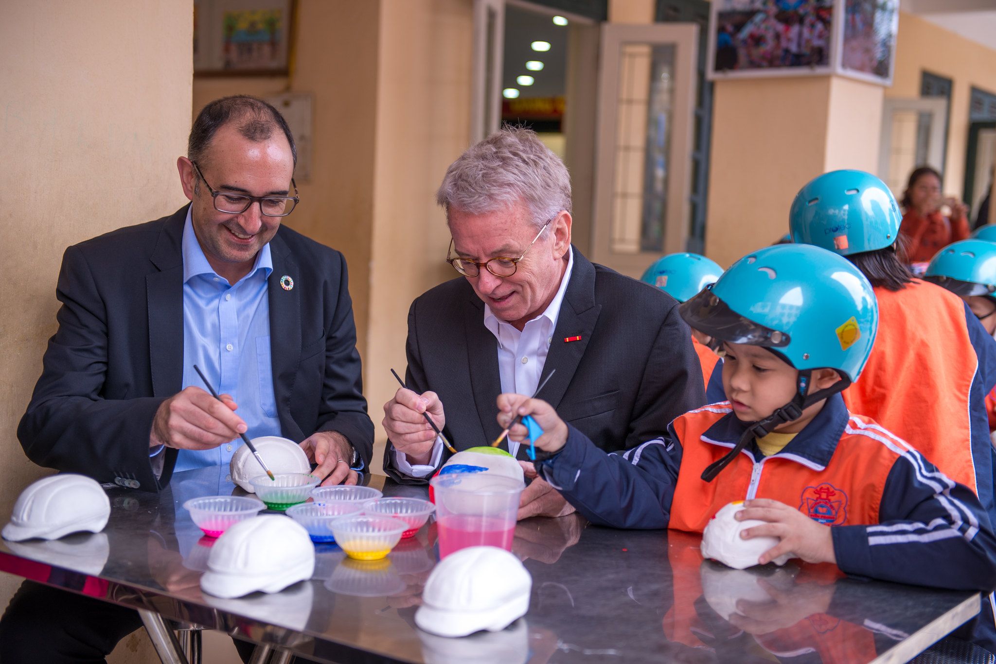 Saul Billingsley, Executive Director of the FIA Foundation, and Greig Craft, President of AIP Foundation, paint helmet sculptures with students as part of activities for the “Fun with Traffic Safety” Day.