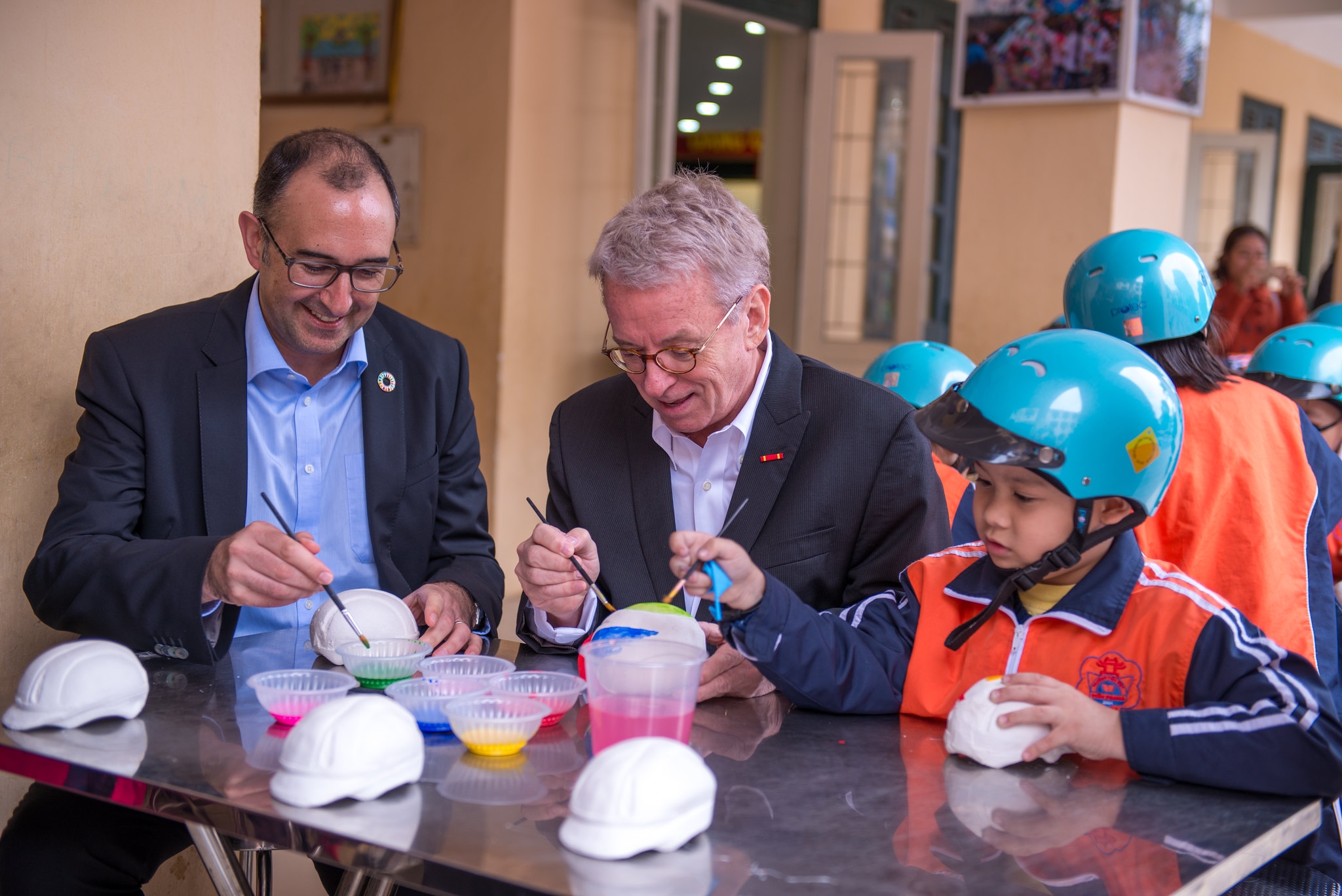 Saul Billingsley, Executive Director of the FIA Foundation, and Greig Craft, President of AIP Foundation, paint helmet sculptures with students as part of activities for the “Fun with Traffic Safety” Day.