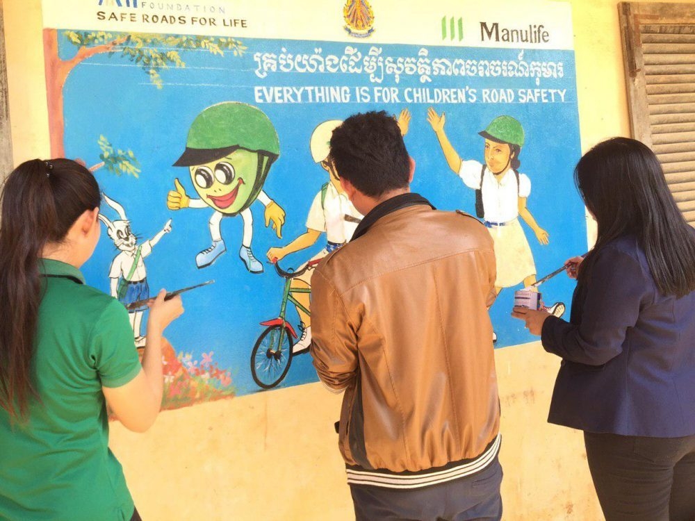 Volunteers from Manulife Cambodia and AIP Foundation staff paint a mural which reads, "Everything is for children's road safety," on school walls.