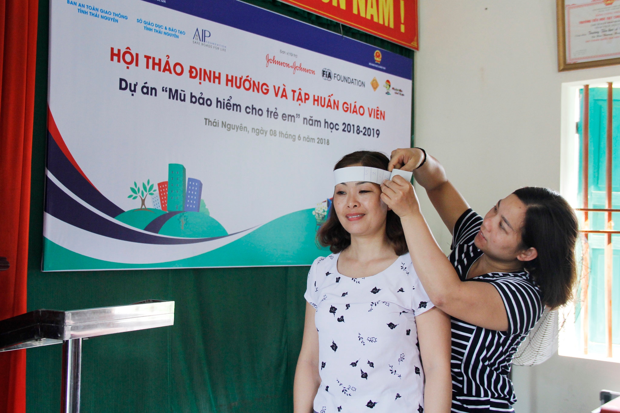 A teacher practices measuring helmet size using a paper ruler.