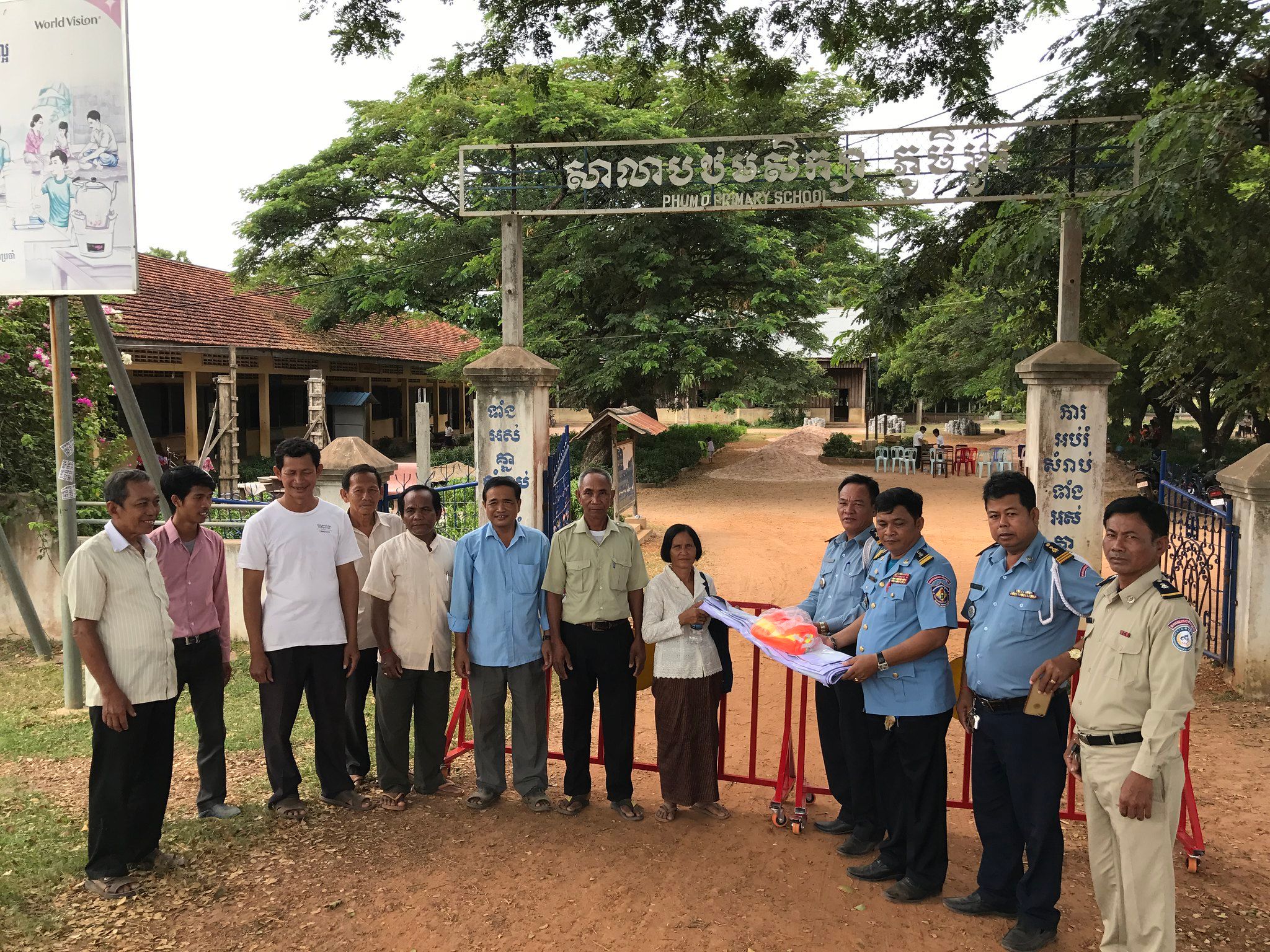 Local stakeholders, including members of the commune board, local police, and parents, pose with Phum O Primary School’s new reflective jackets and traffic barrier.