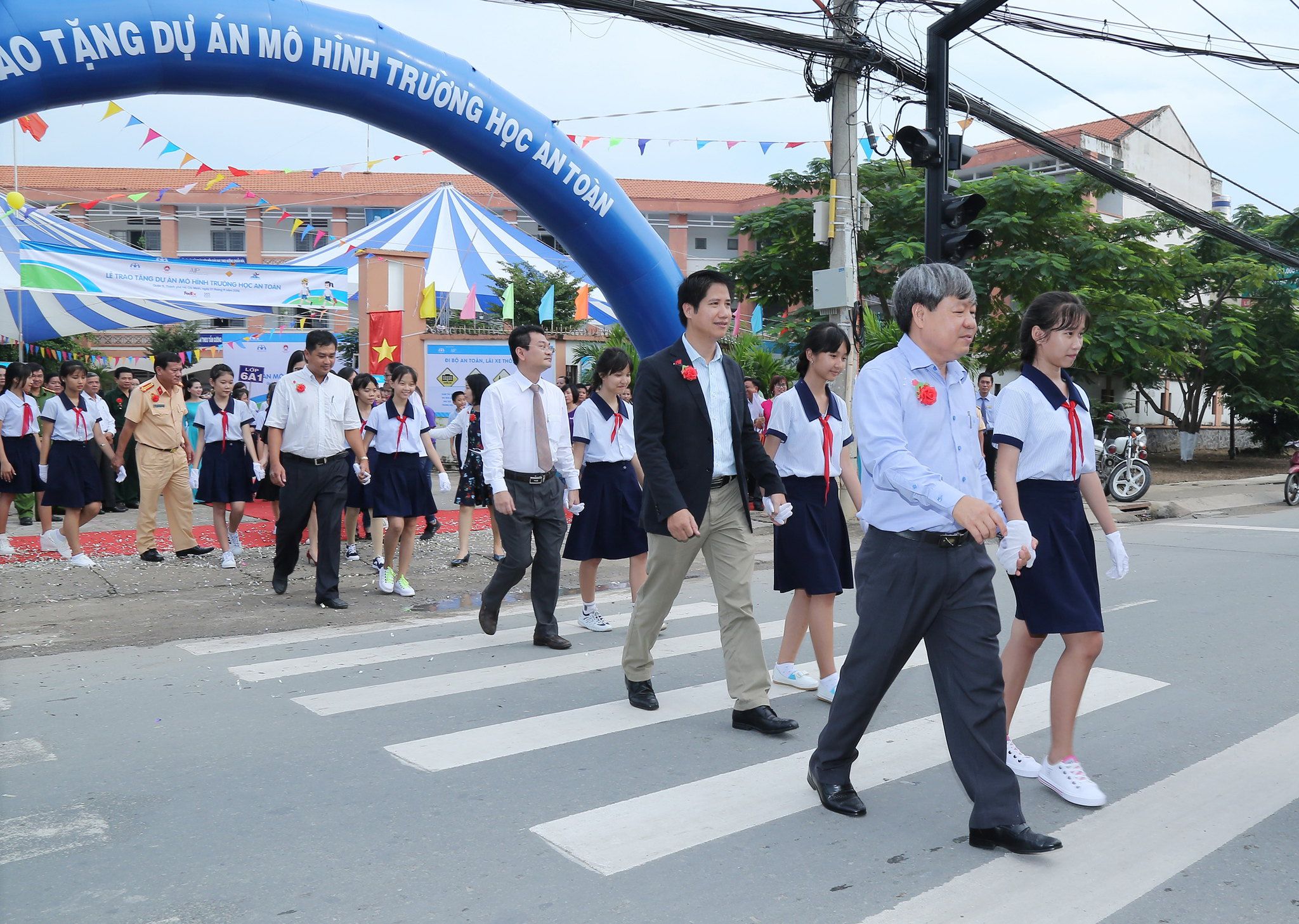 Stakeholder representatives, including Mr. Thang Dao, FedEx’s Senior Manager of Indochina and Country Manager of Vietnam (center), and Mr. Nguyen Ngoc Tuong, Deputy Director of the Standing Committee of the Ho Chi Minh City Traffic Safety Committee (right), join students in using the new push-button pedestrian cross light in front of Long Truong Secondary School.