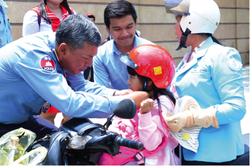 A law enforcement official in Cambodia teaches a young girl how to properly wear a helmet. The mandatory passenger helmet law began to be enforced in January 2016.