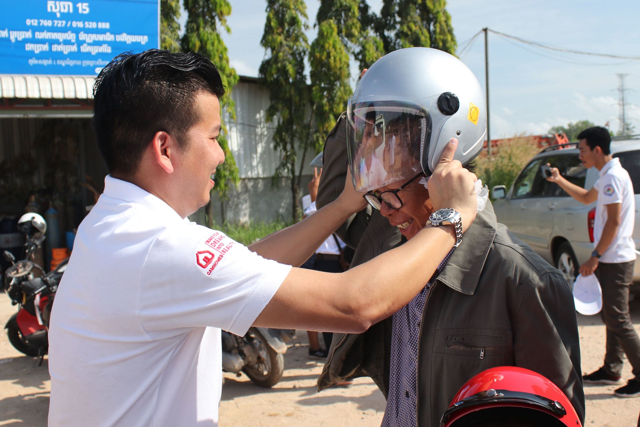 12 November, 2018 – Sihanoukville Camhomes staff shows adult motorcyclist how to correctly wear a helmet