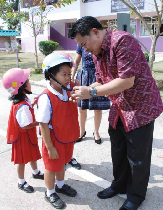 Principal Tanongsak Haprom helps students put on their helmets at school.