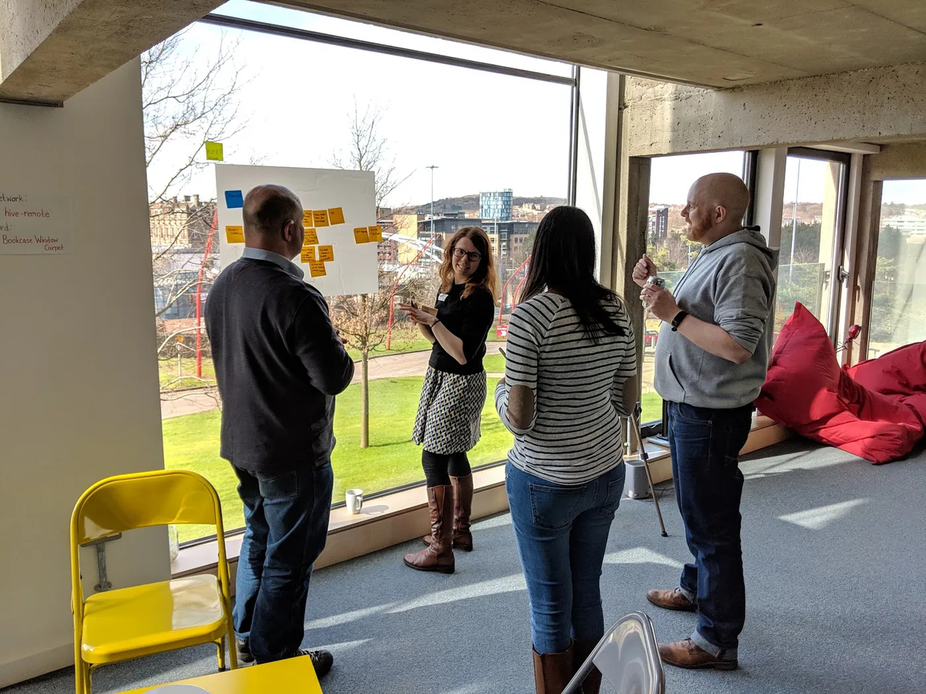 People stood up looking at a whiteboard holding sticky notes during a workshop