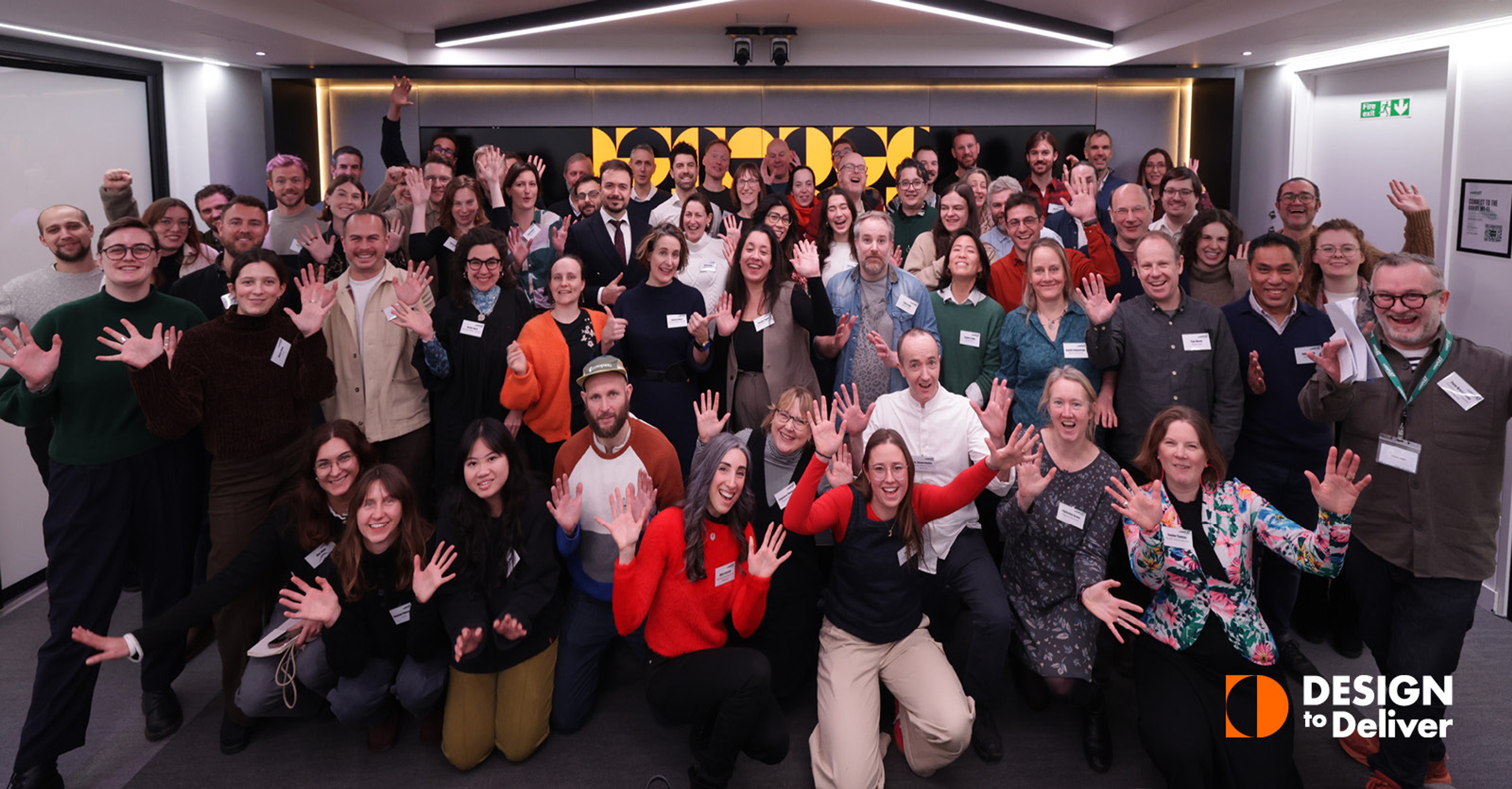 An image of a group of people smiling with their hands raised from the Design to Deliver programme. Accompanied by an orange and white Design to Deliver programme logo in the bottom left of the image