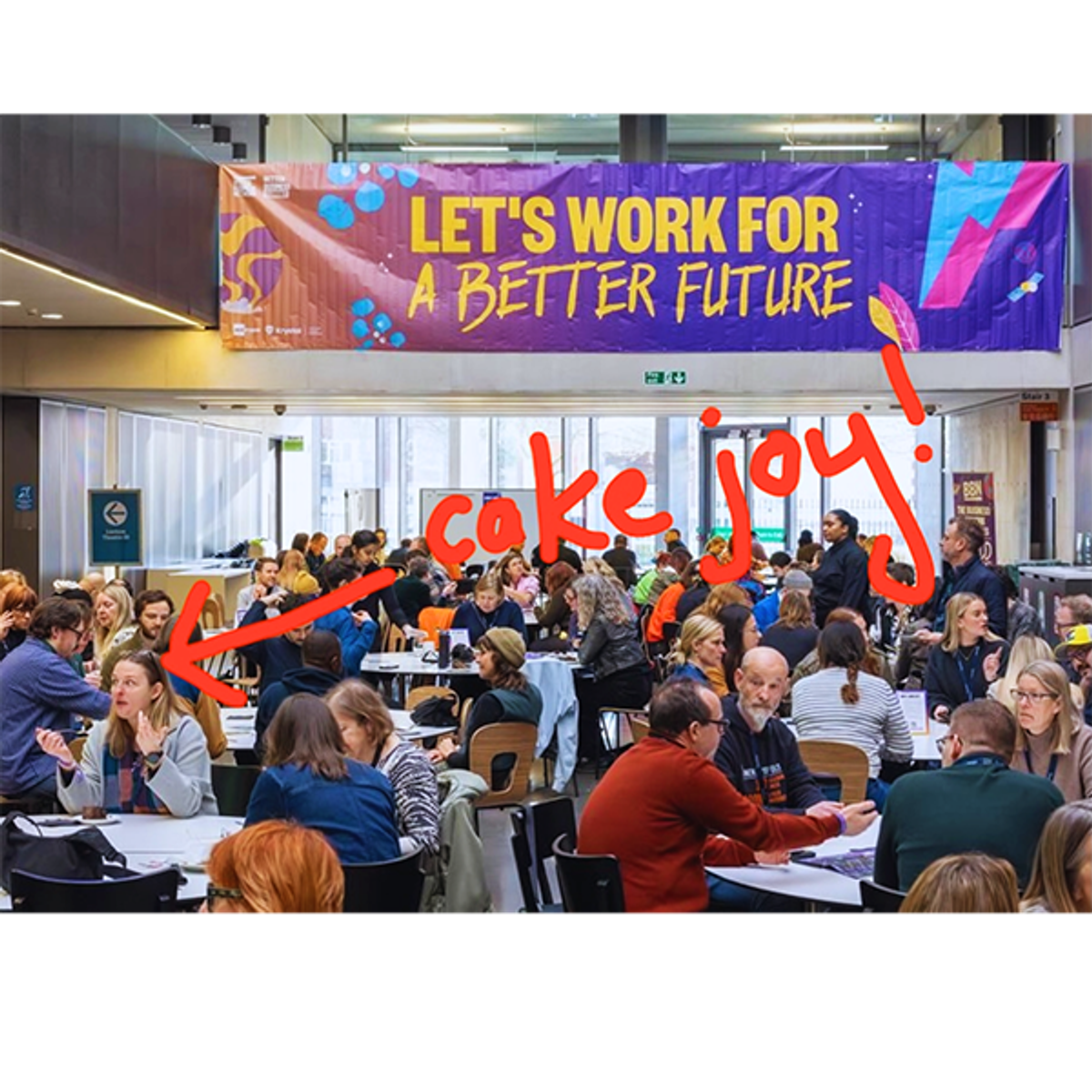 A picture of a lunch hall with people enjoying their food. With the writing 'Lets work for a better future' and a red hand drawn arrow pointing to Liz Hnat which says, 'Cake Joy!'