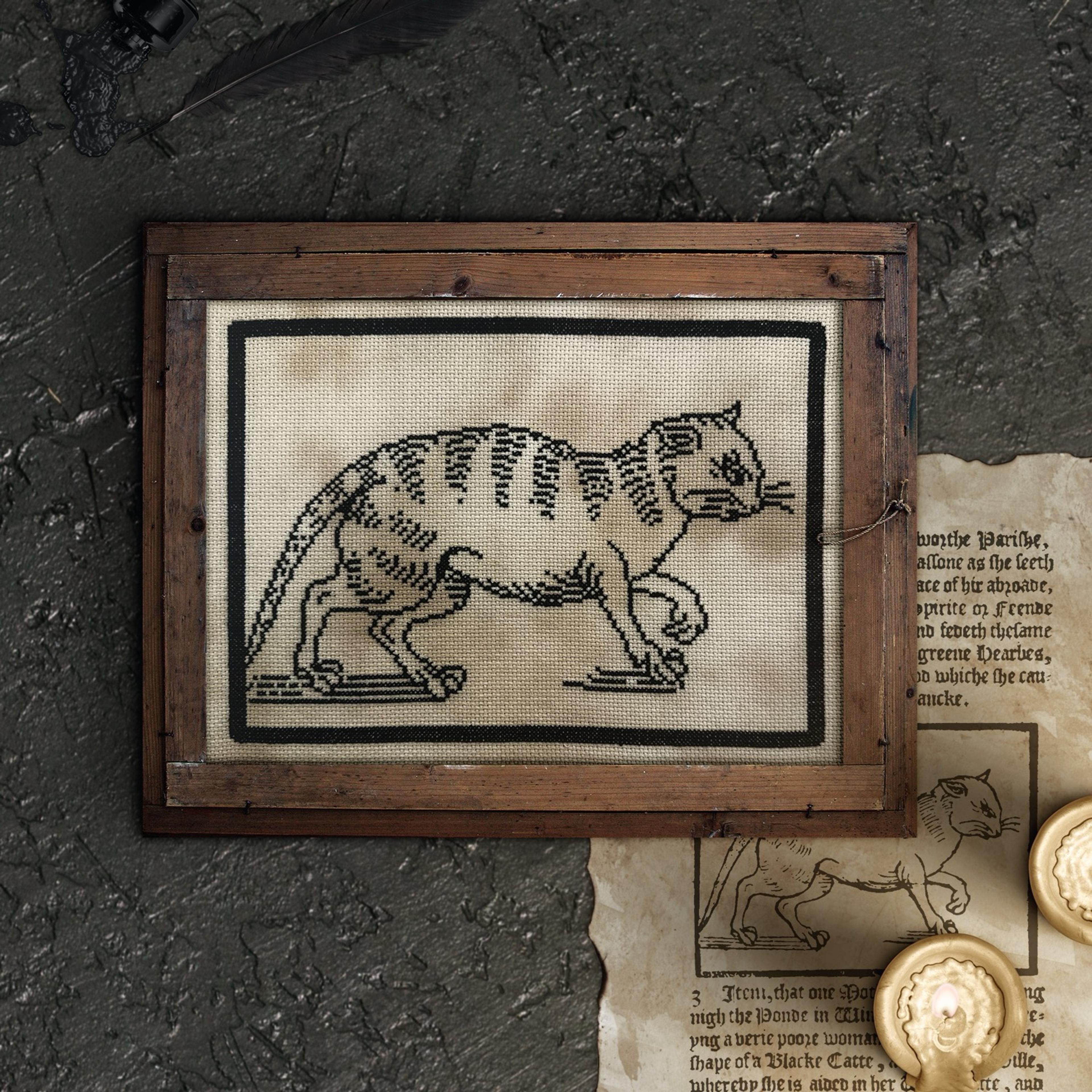 Framed cross stitch of a cat head in the style of a 16th century woodcut.