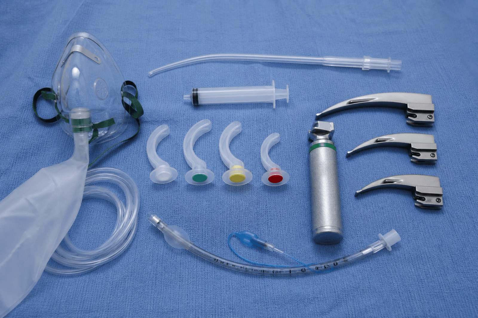 Oxygen mask, suction tip, and airway tray components on a blue sterile towel.