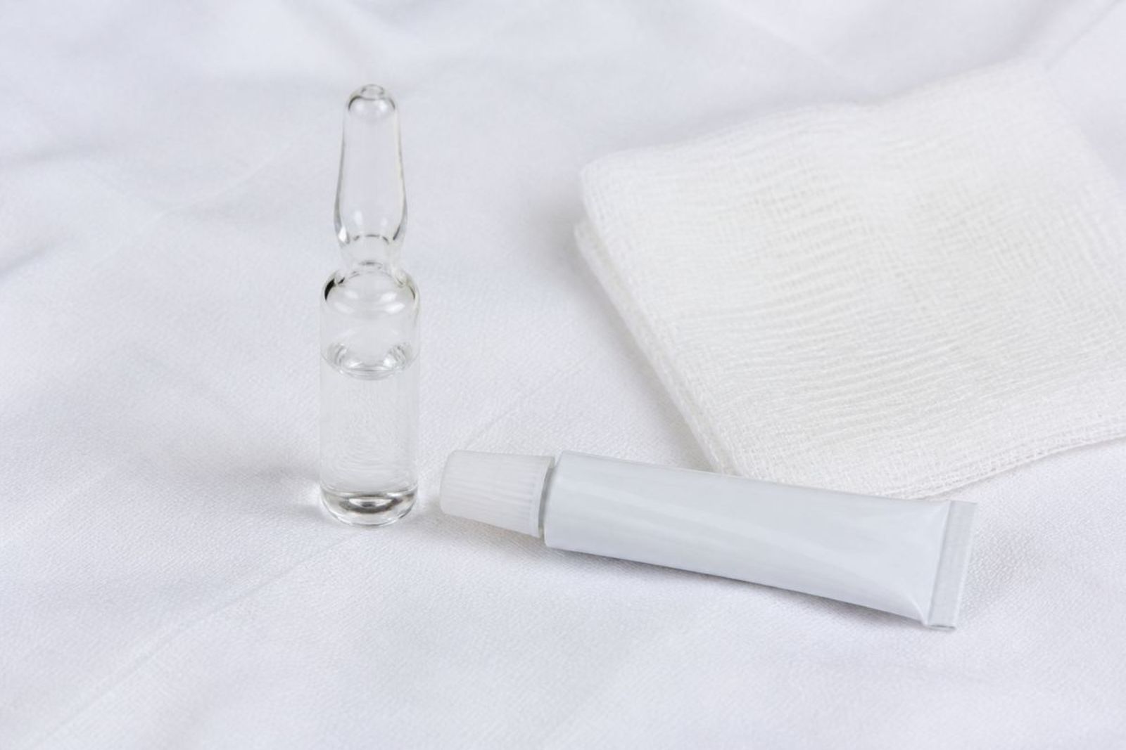 Unmarked injectable ampule beside a small ophthalmic ointment tube and sterile gauze on white linen.