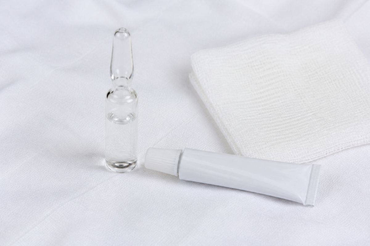 Unmarked injectable ampule beside a small ophthalmic ointment tube and sterile gauze on white linen.