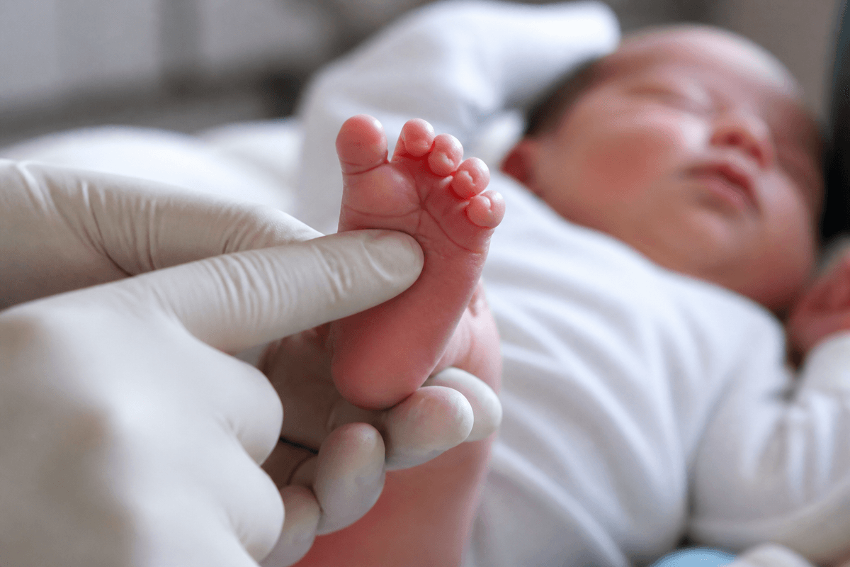 Gloved hand eliciting a plantar grasp reflex on a newborn foot.
