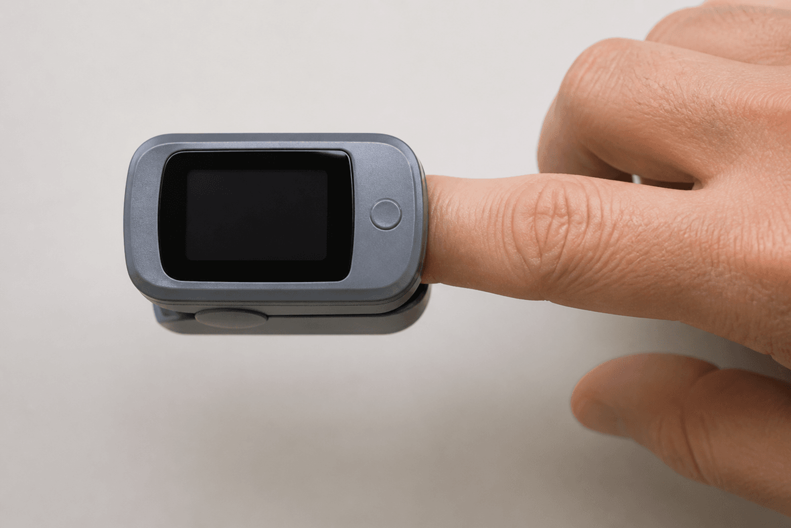 Gray fingertip pulse oximeter clipped on an adult index finger with a blank display.