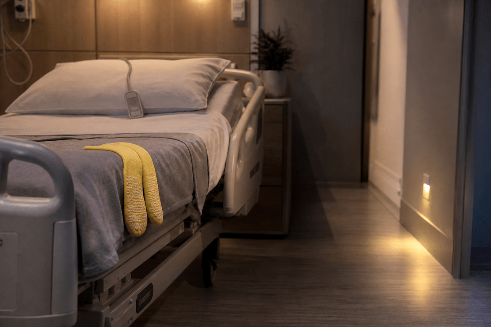 Hospital bed with yellow non-slip socks, call light on the pillow, clear floor path, and a night light.