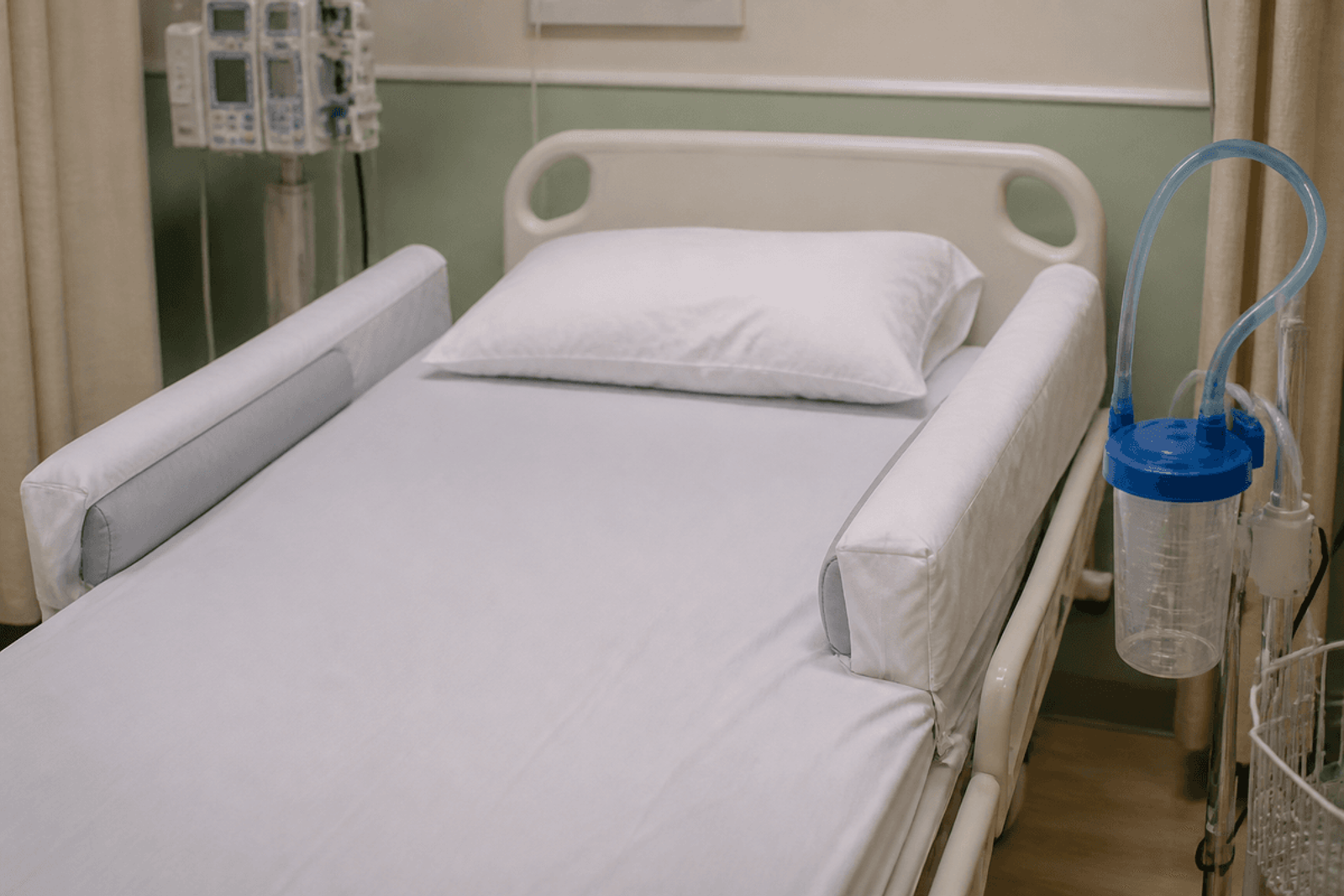 Padded side rails and suction staged at an empty hospital bedside.