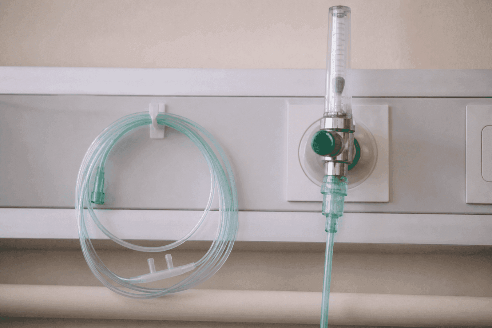 Nasal cannula coiled beside a wall oxygen flowmeter in a hospital room.