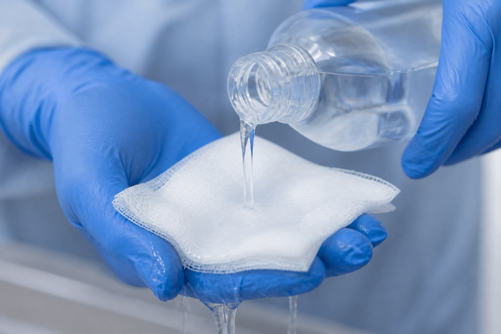 Gloved hands pouring cool saline onto clean gauze.
