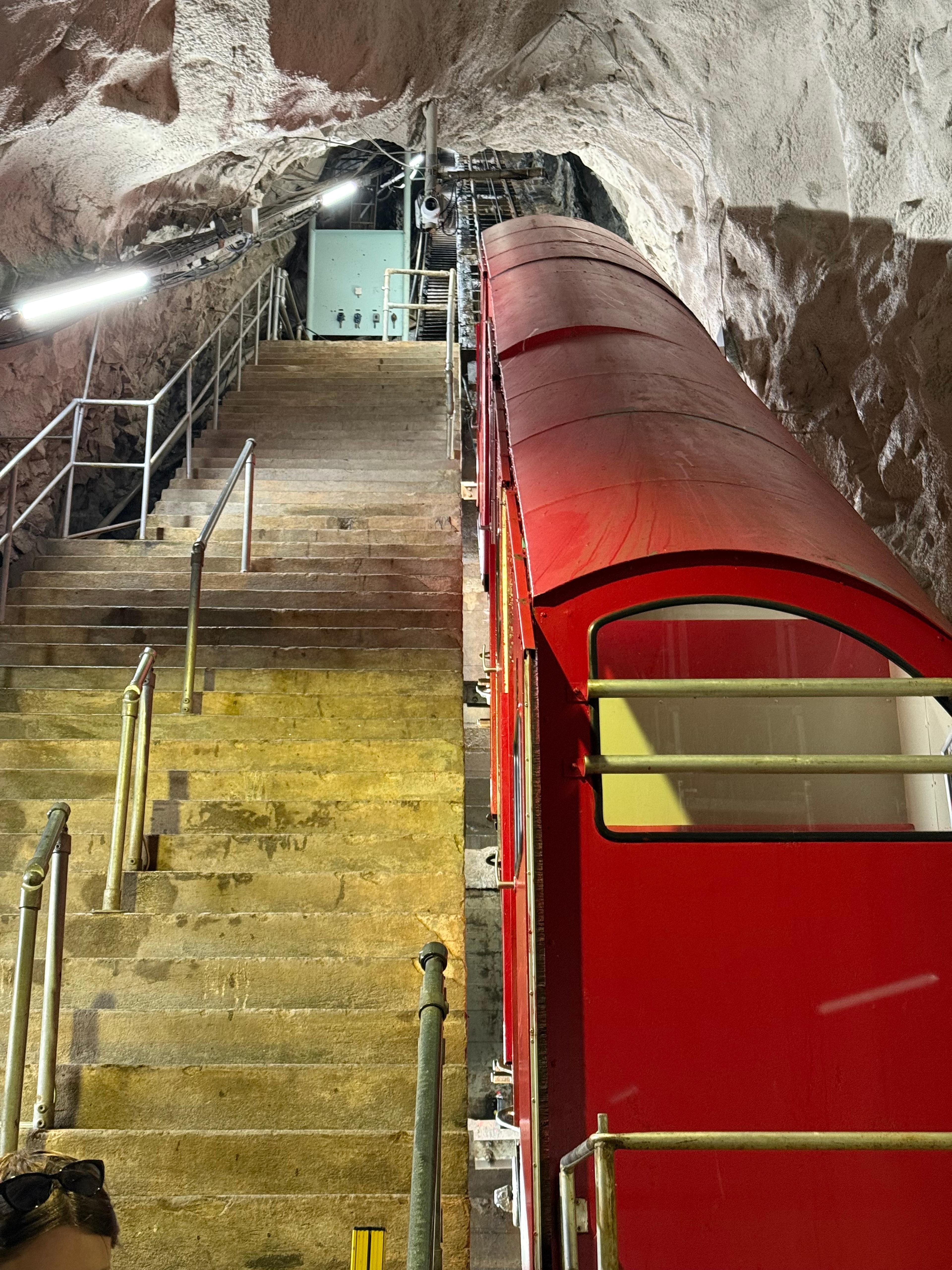 Rød vogn i en bratt tunnel inne i fjellet, med trapp ved siden av.