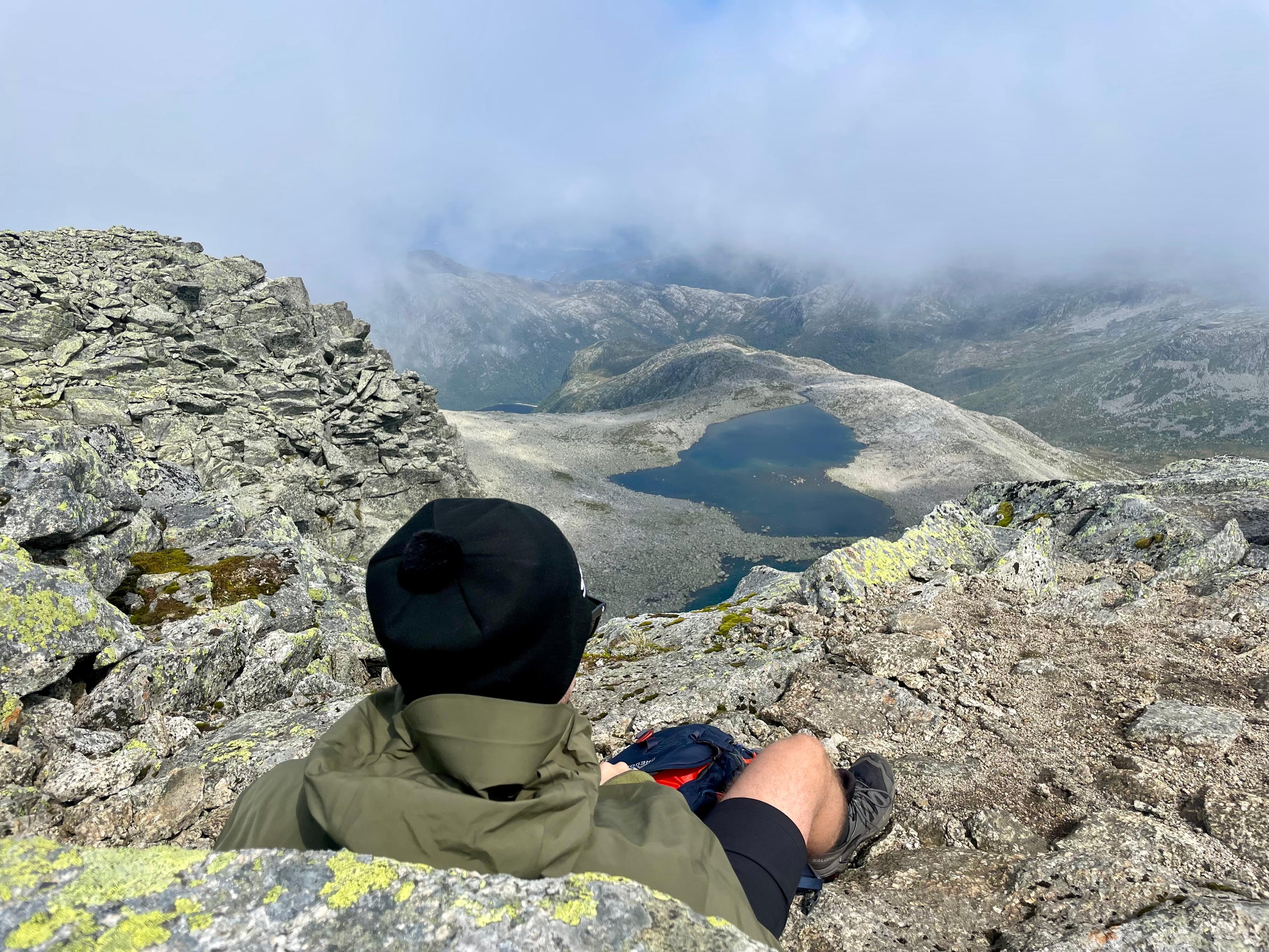 Turgåer i tåka på toppen ser ned på et fjellvann