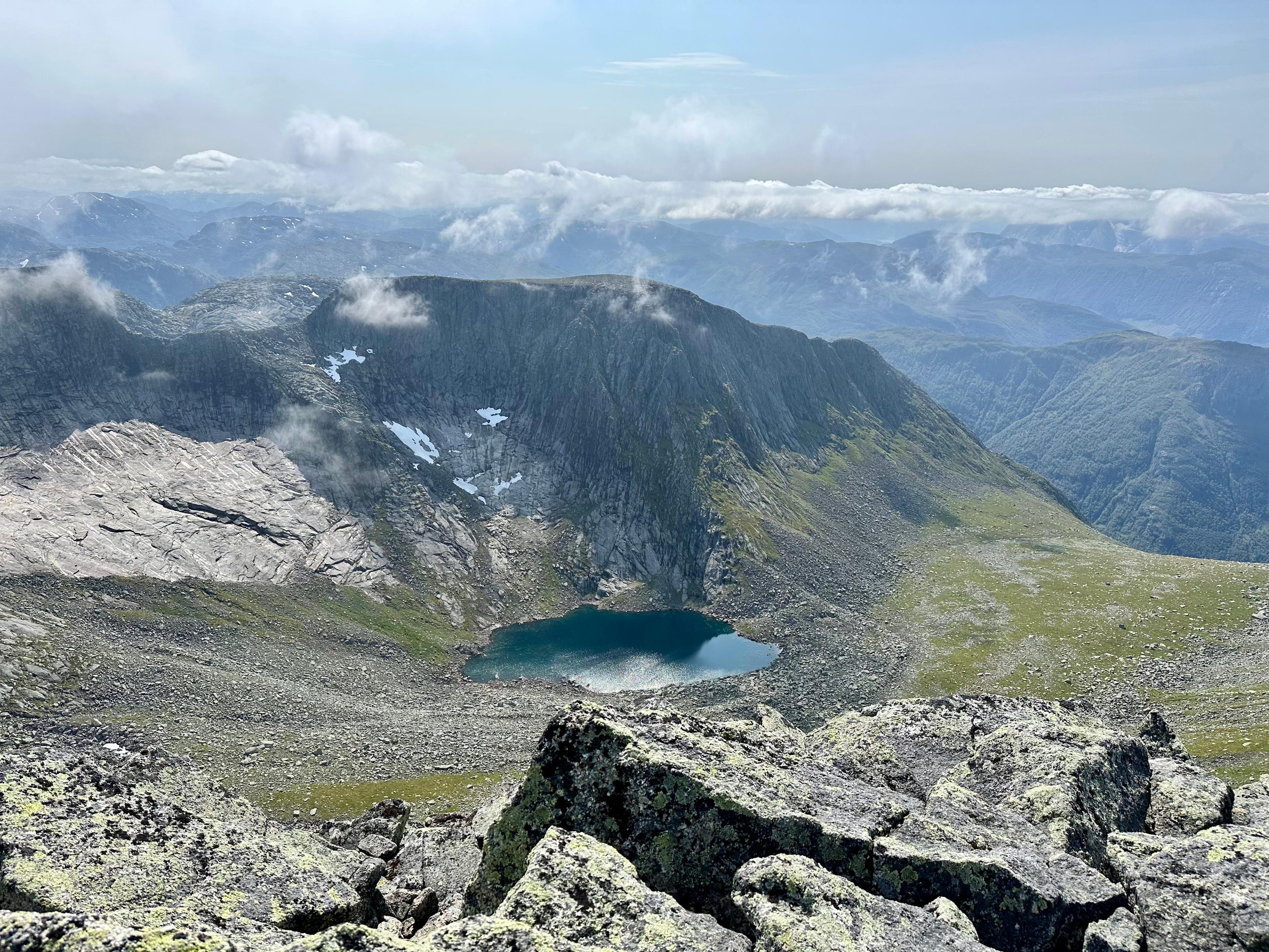 Fjellvann med snøflekker under en bratt egg, sett fra toppen av Melderskin