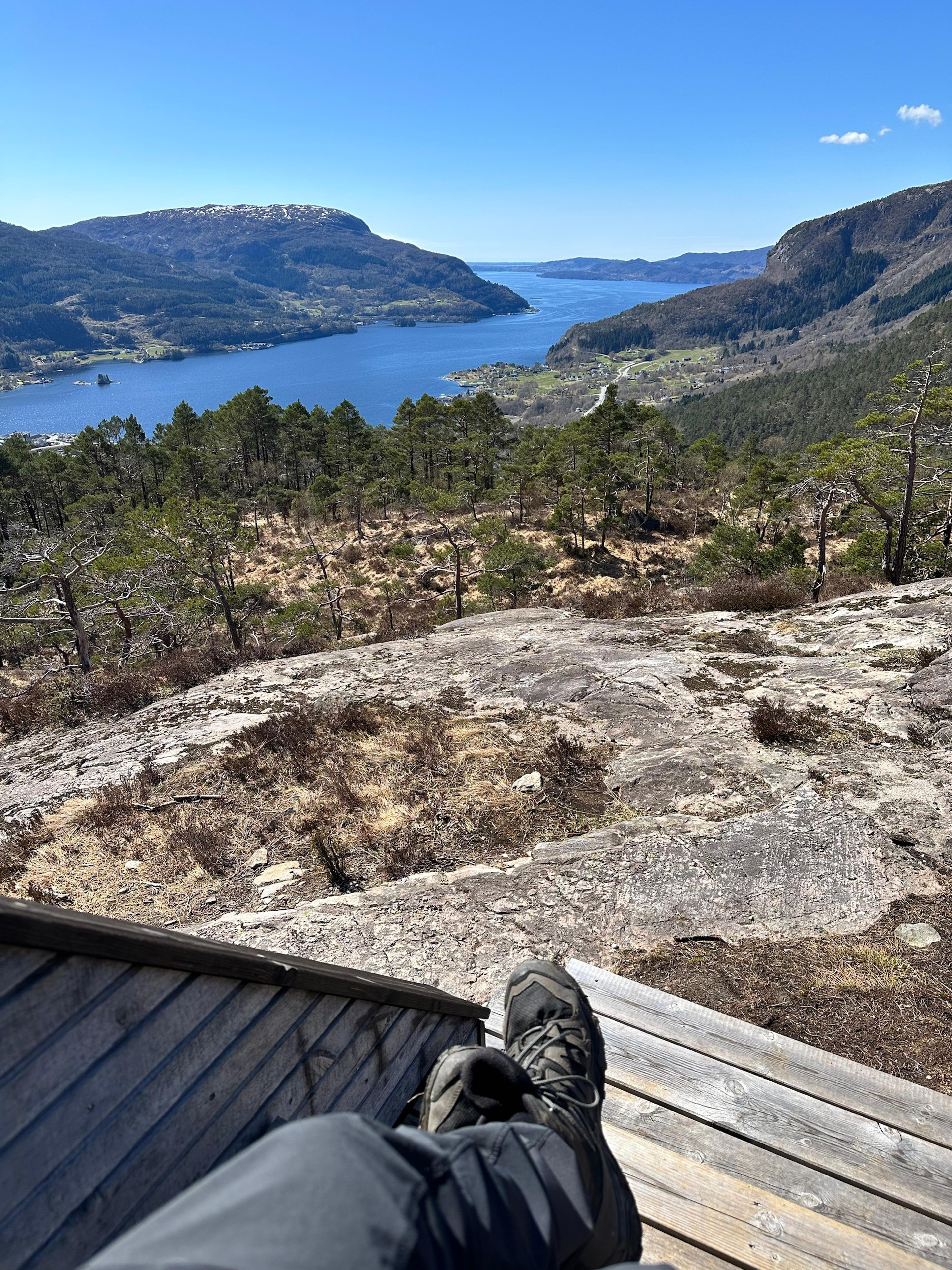Føtter i turstøvler på terrassen ved hytten, med utsikt over fjorden nedenfor.