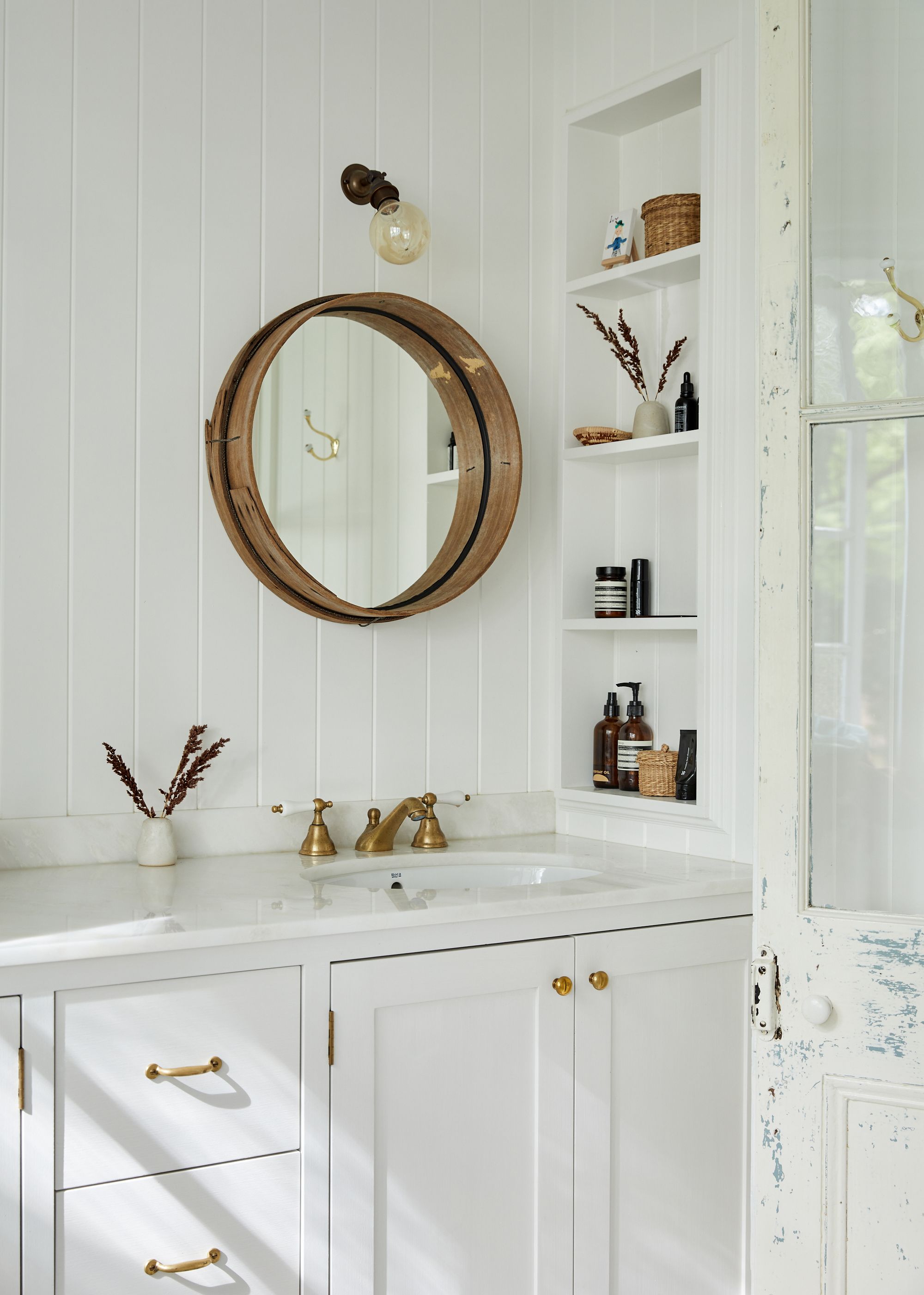 A country-style rustic white bathroom with a featured gold circular mirror 