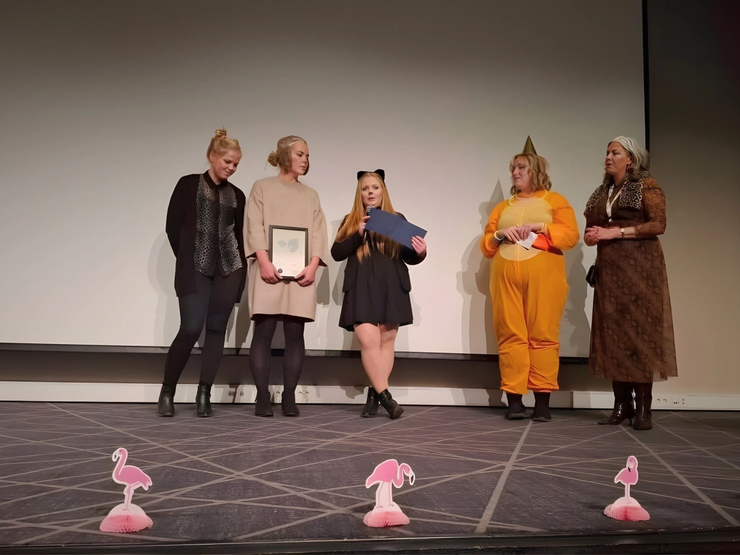 Fem ansatte fra EMPET Askim står på scenen under utdelingen av prisen Årets Arbeidsplass 2025 fra Norsk dyrepleier- og assistentforening (NDAF). De holder diplom og blomster mens de smiler mot publikum.