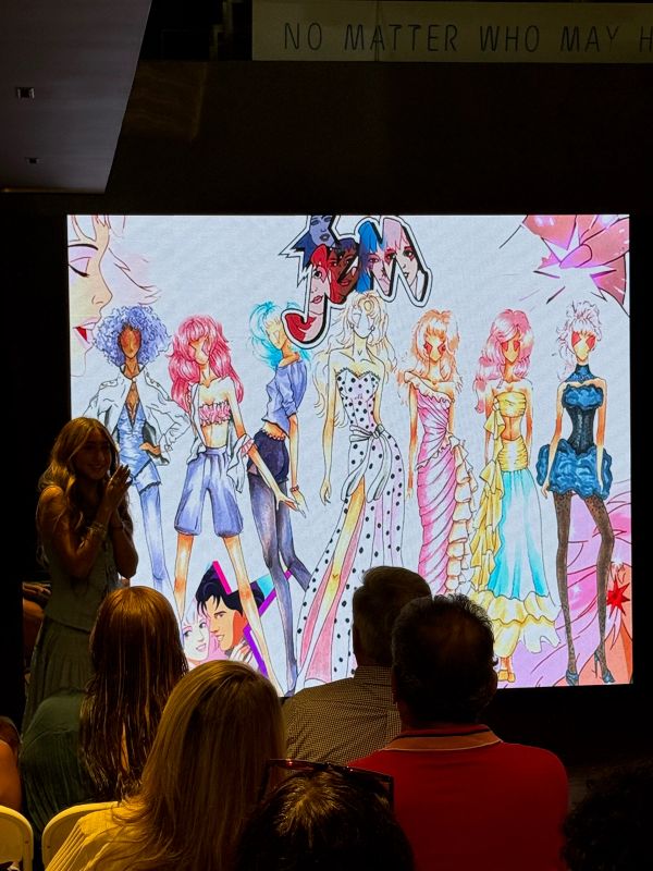 Presenting my Jem and the Holograms-inspired fashion project to an audience, with a colorful concept illustration displayed on a large screen.
