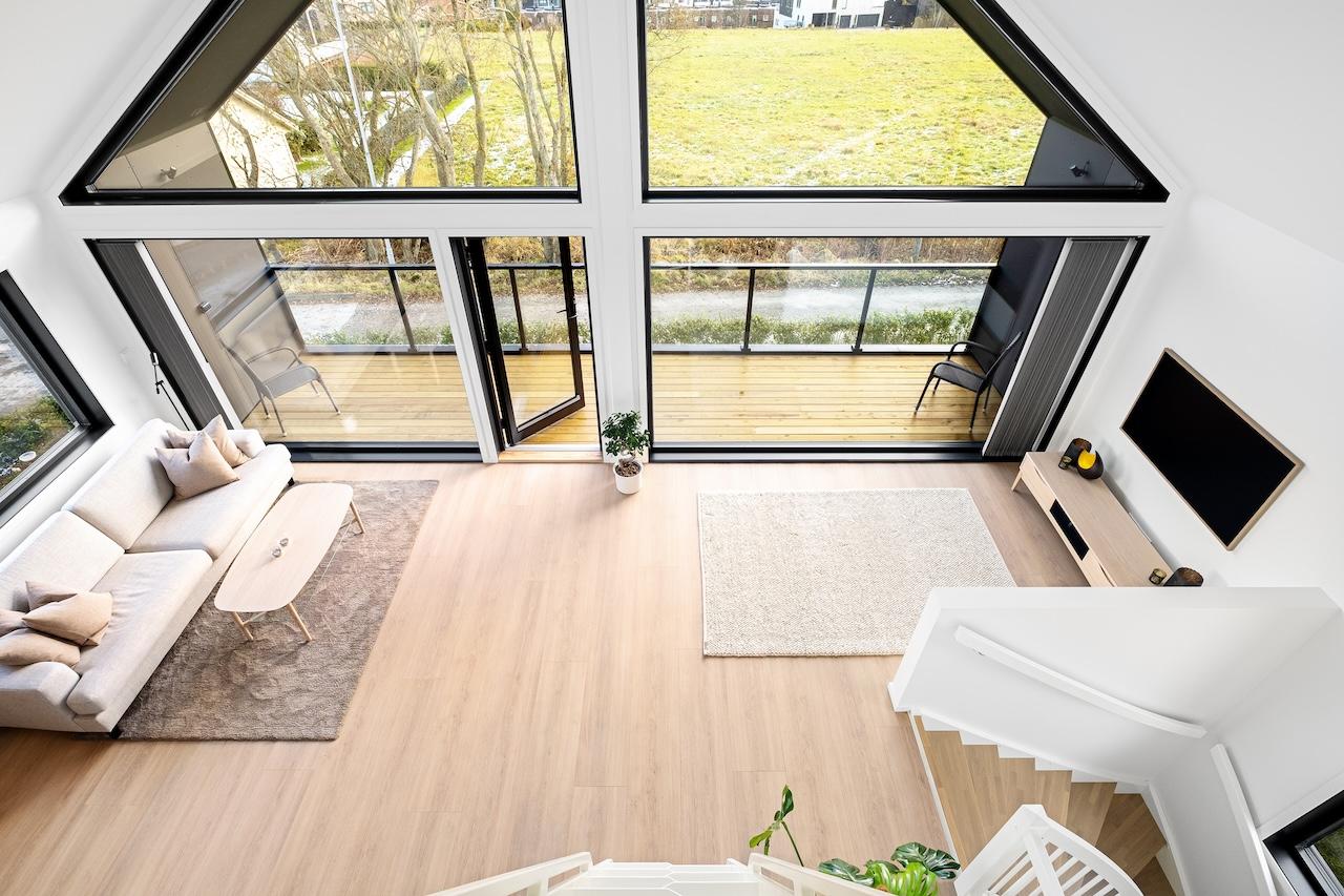 Man ser ned i stuen fra hemsen. Lysflommen fra store vinduer definerer stuen i hjemmet.