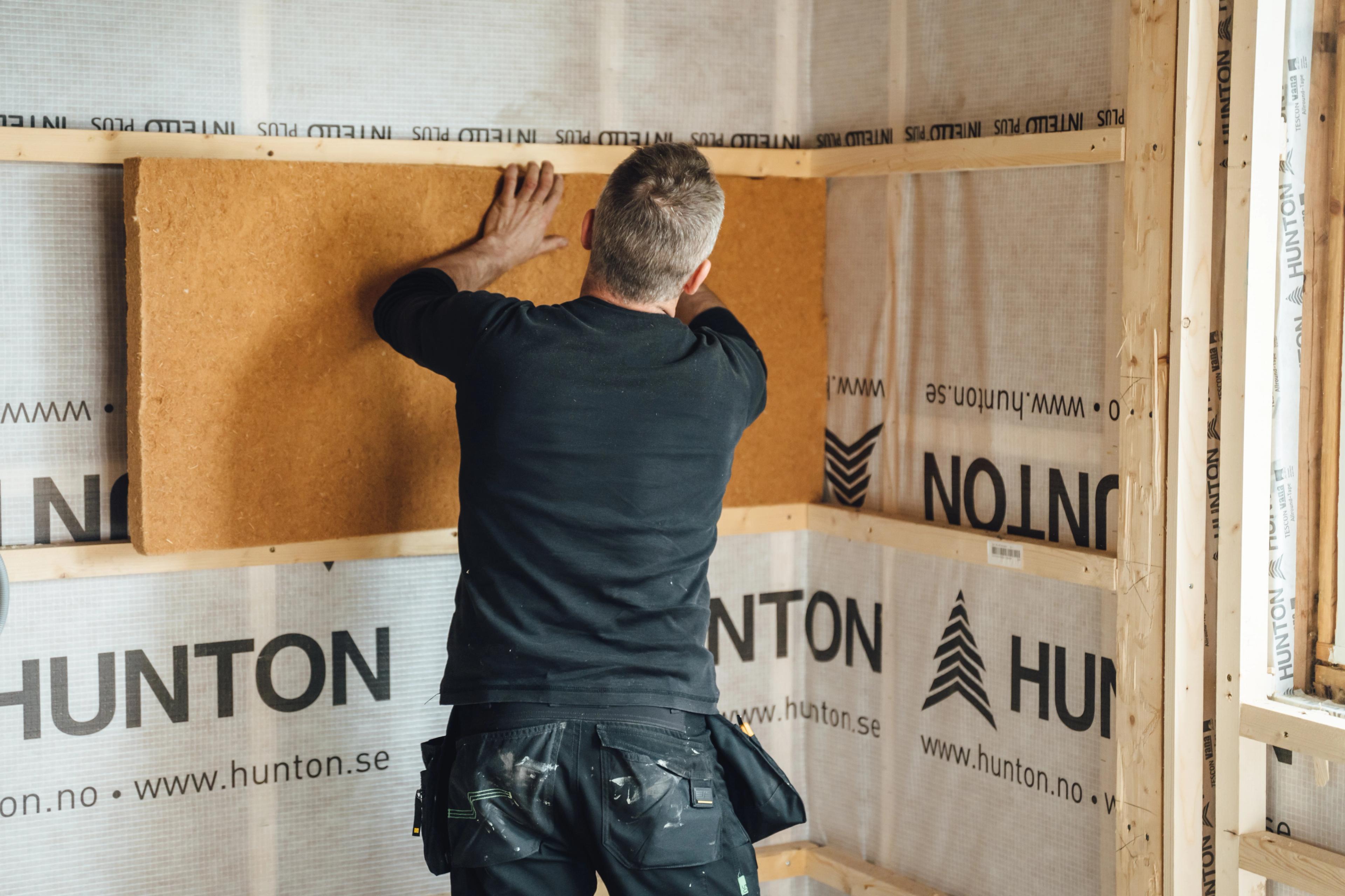 En mann dytter på plass isolasjon i en vegg