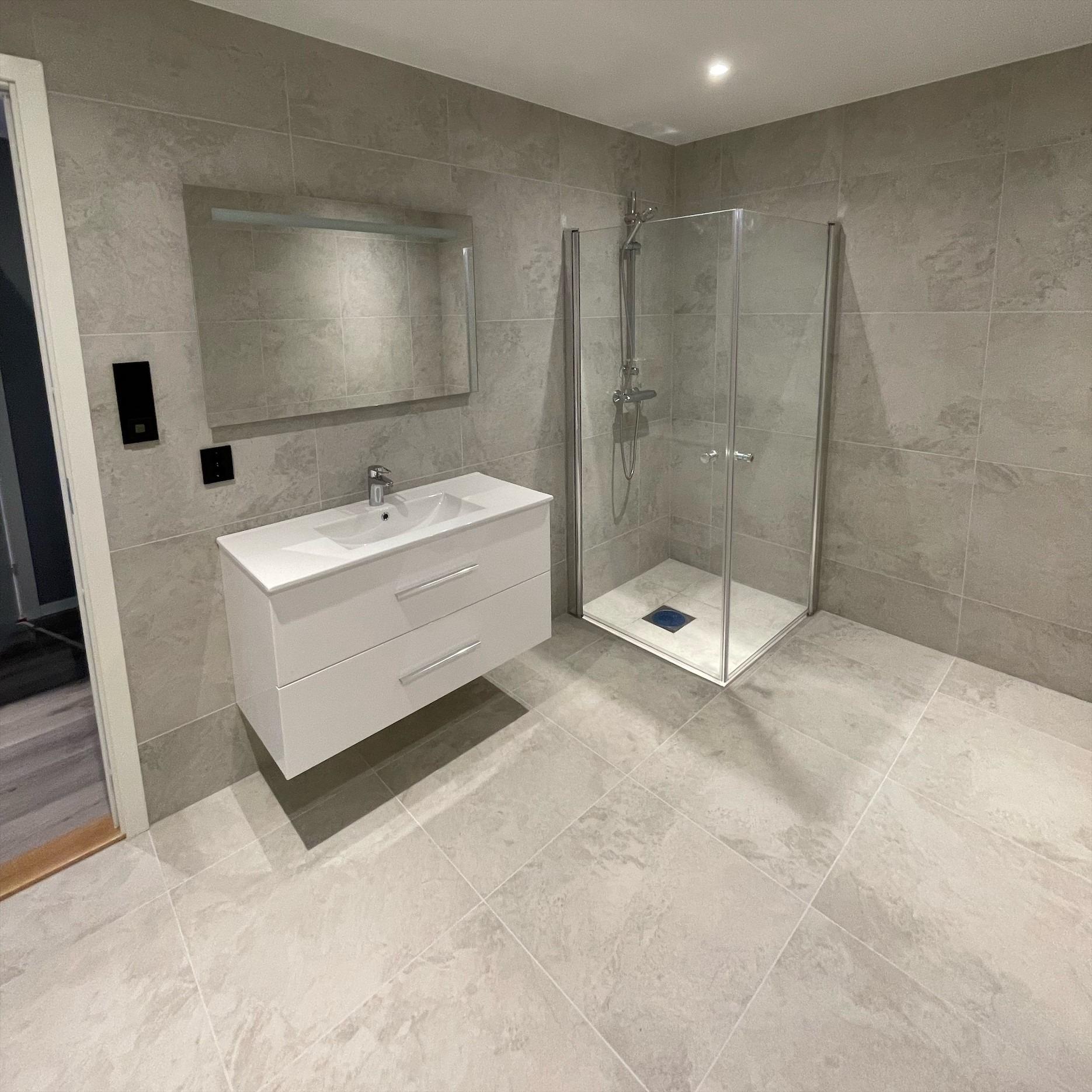 BADEROM 1.ETASJE: Lyse store fliser på gulv og vegg med belysning i speil og stander innredning.