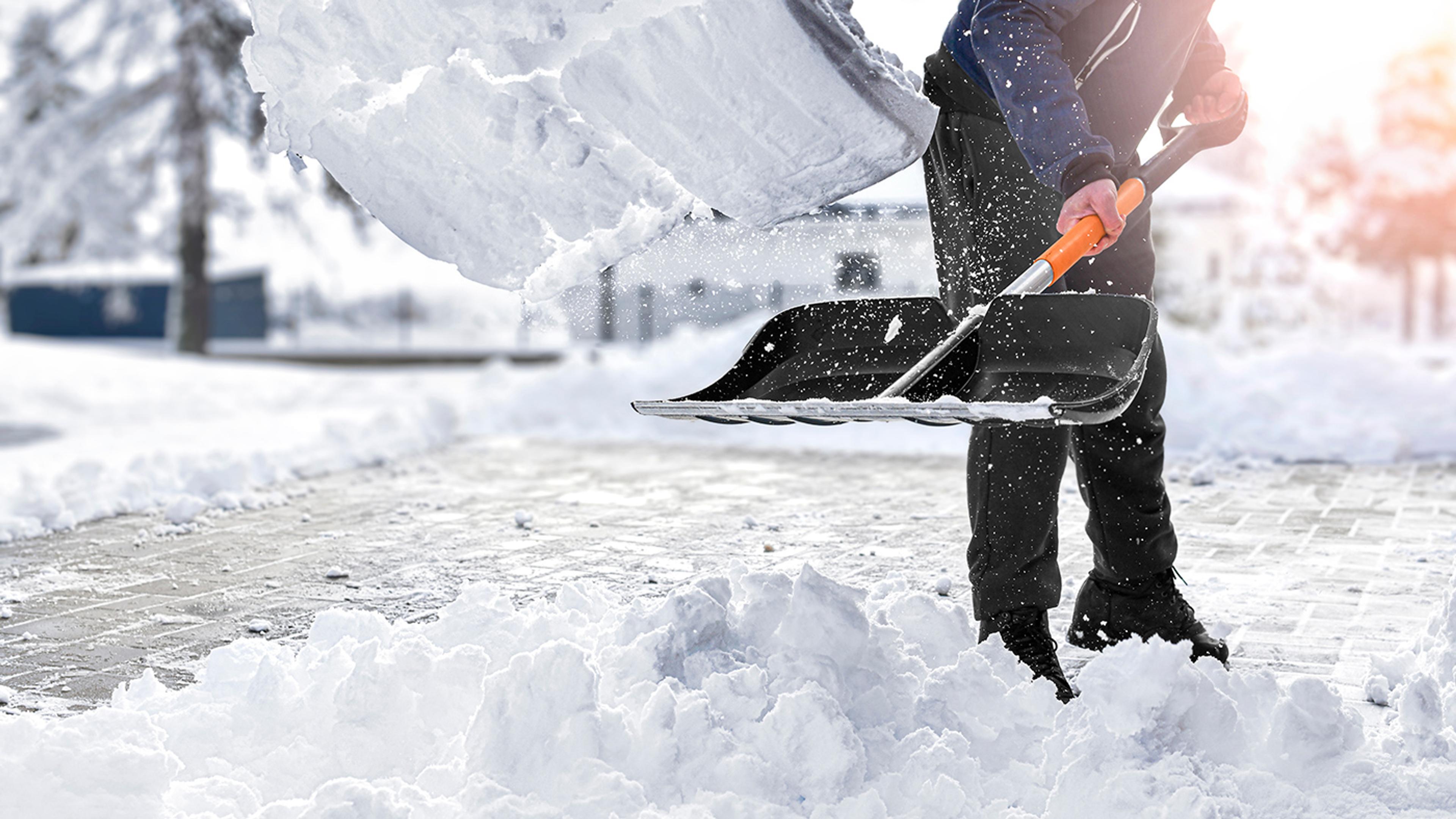 En person skottar snö med en svart och orange snöskyffel och lyfter en stor hög snö