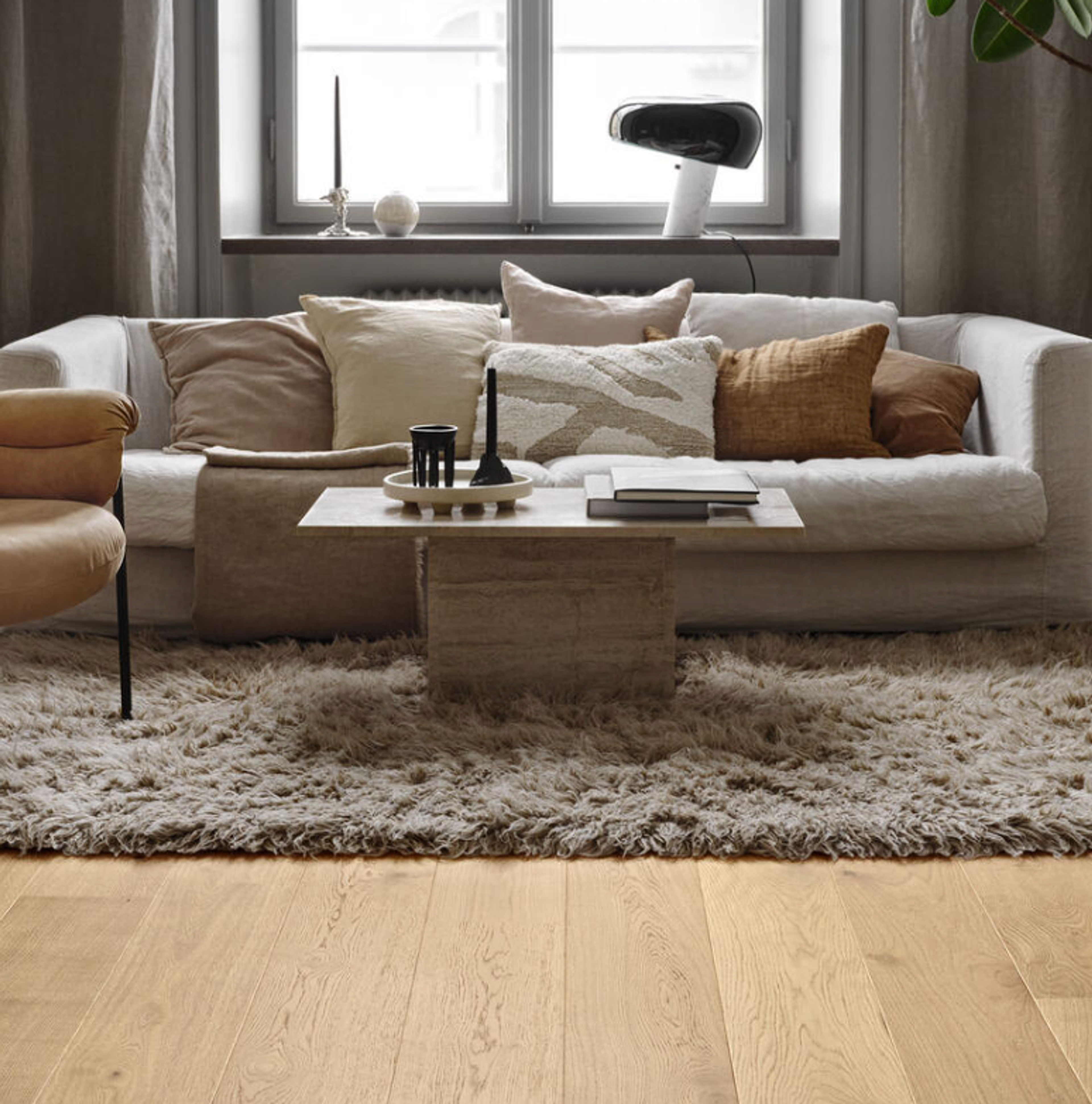 A cozy living room with a white sofa, neutral pillows, a coffee table, a shaggy rug, and light wood floors.