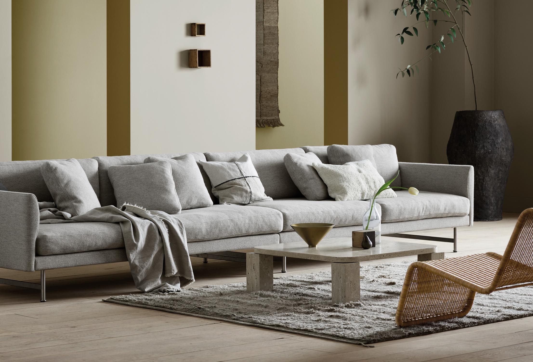 A minimalist living room with a long gray sofa, stone coffee table, and large potted plant.