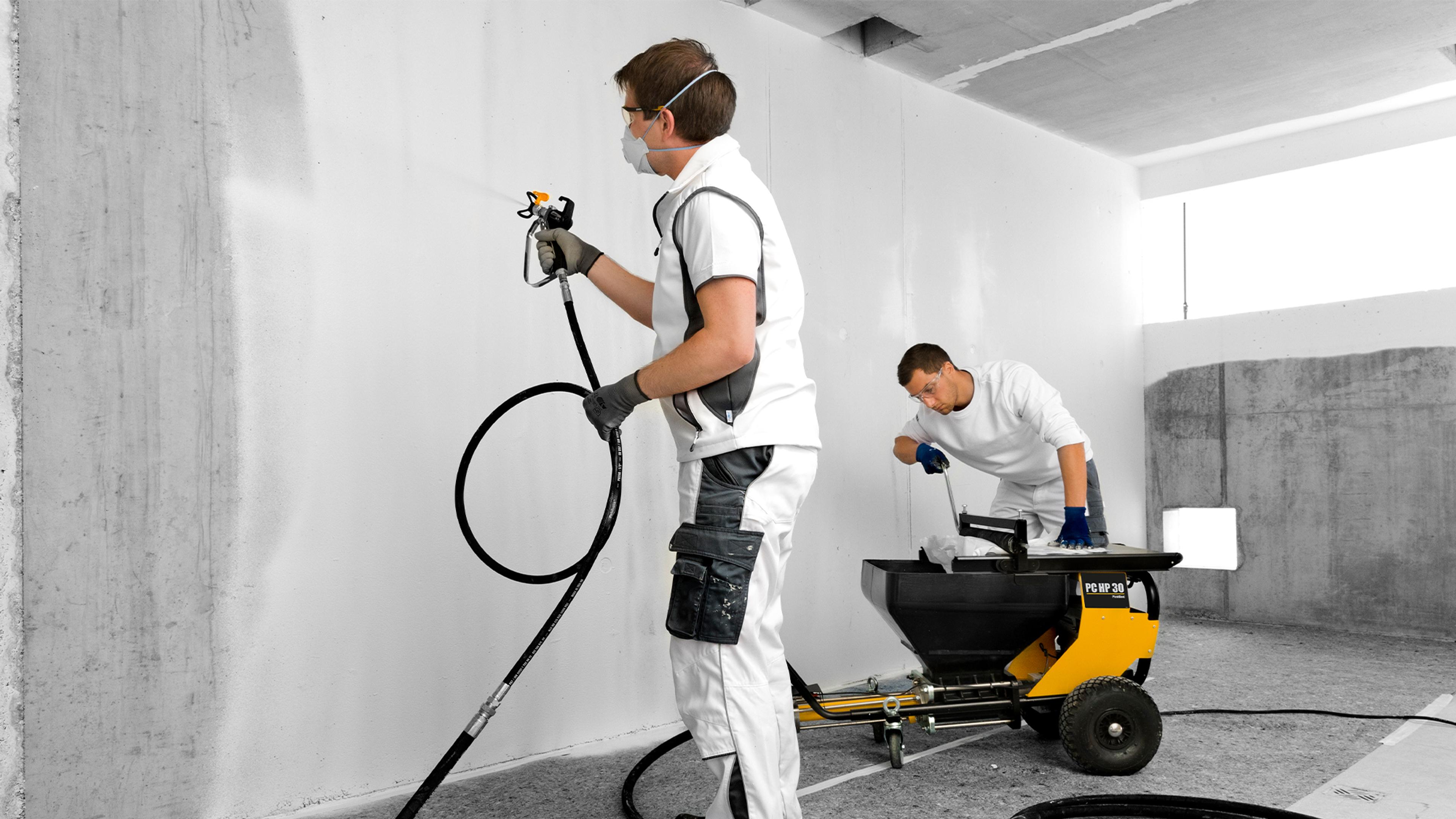 Two workers applying a white coating to a wall using a spray gun and a plastering machine.