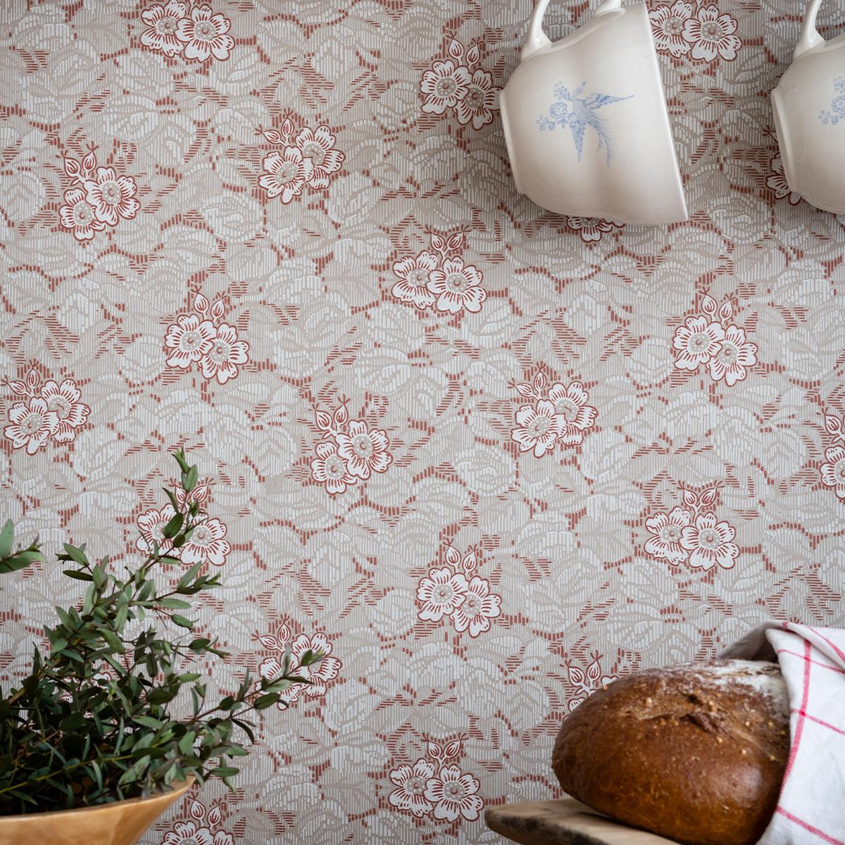 Beige and reddish-brown floral wallpaper behind white mugs, a green plant, and a rustic bread loaf.