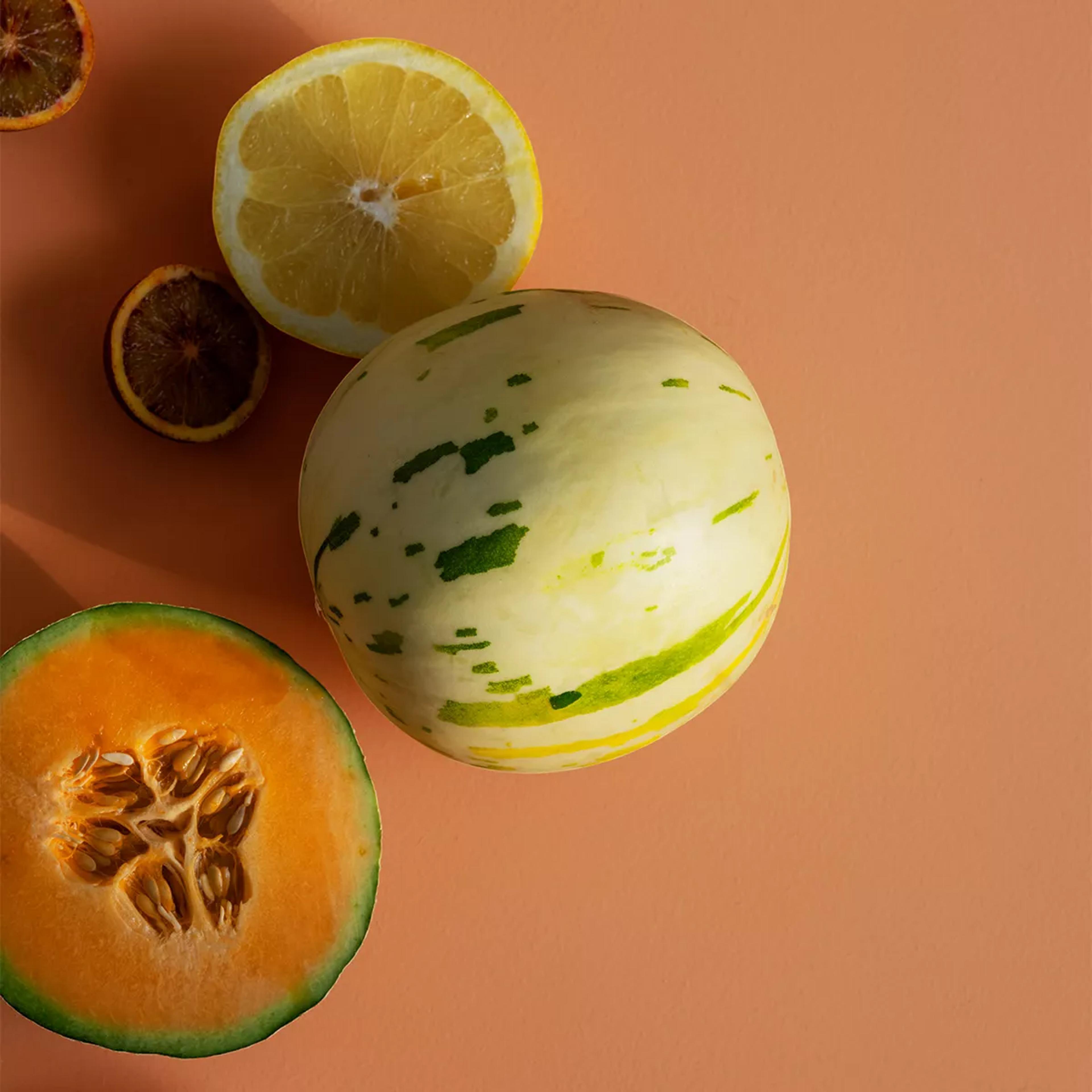 A half lemon, a striped melon, and a half cantaloupe on a peach background.