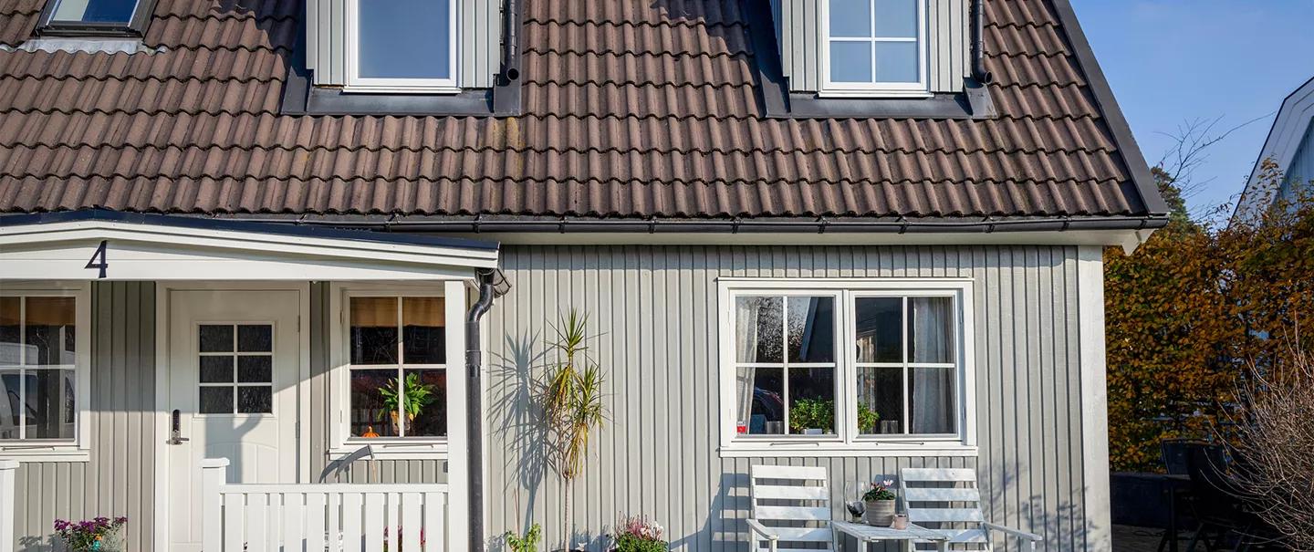 Light grey house with white windows, brown tiled roof, and white outdoor chairs.