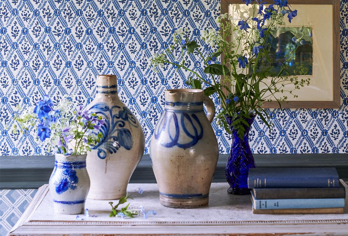 Blue and white room decor featuring rustic pottery, blue flowers, and books against patterned wallpaper.
