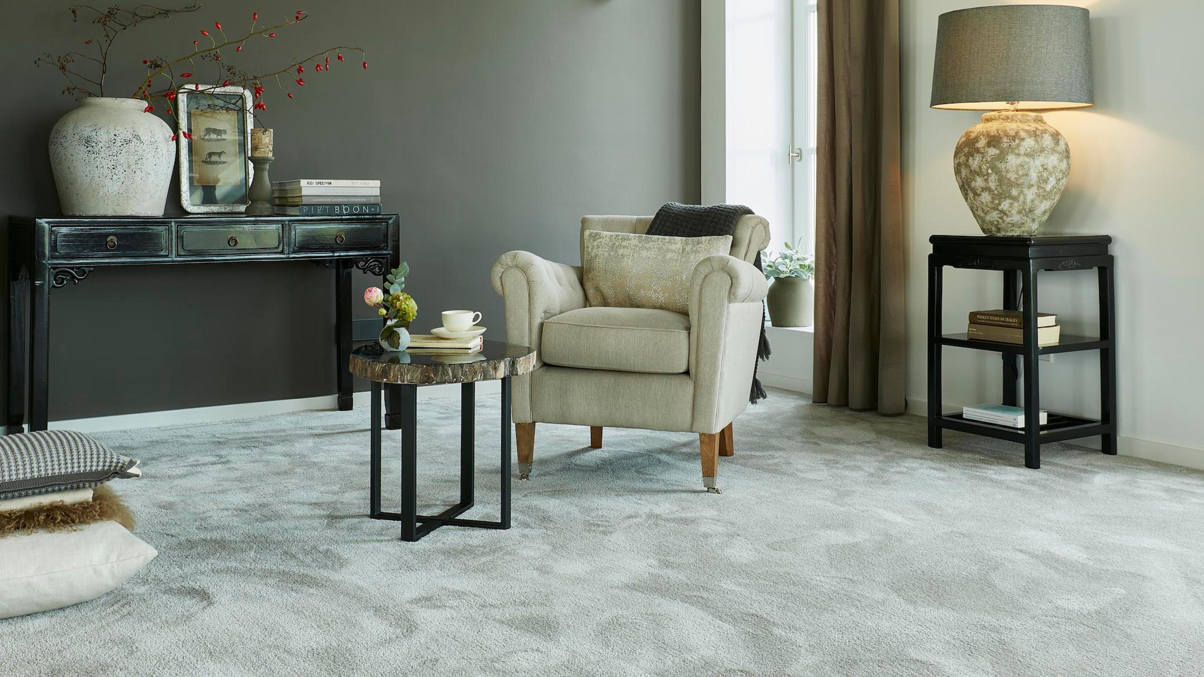A light gray patterned carpet in a living room with a cream armchair and dark wood furniture.
