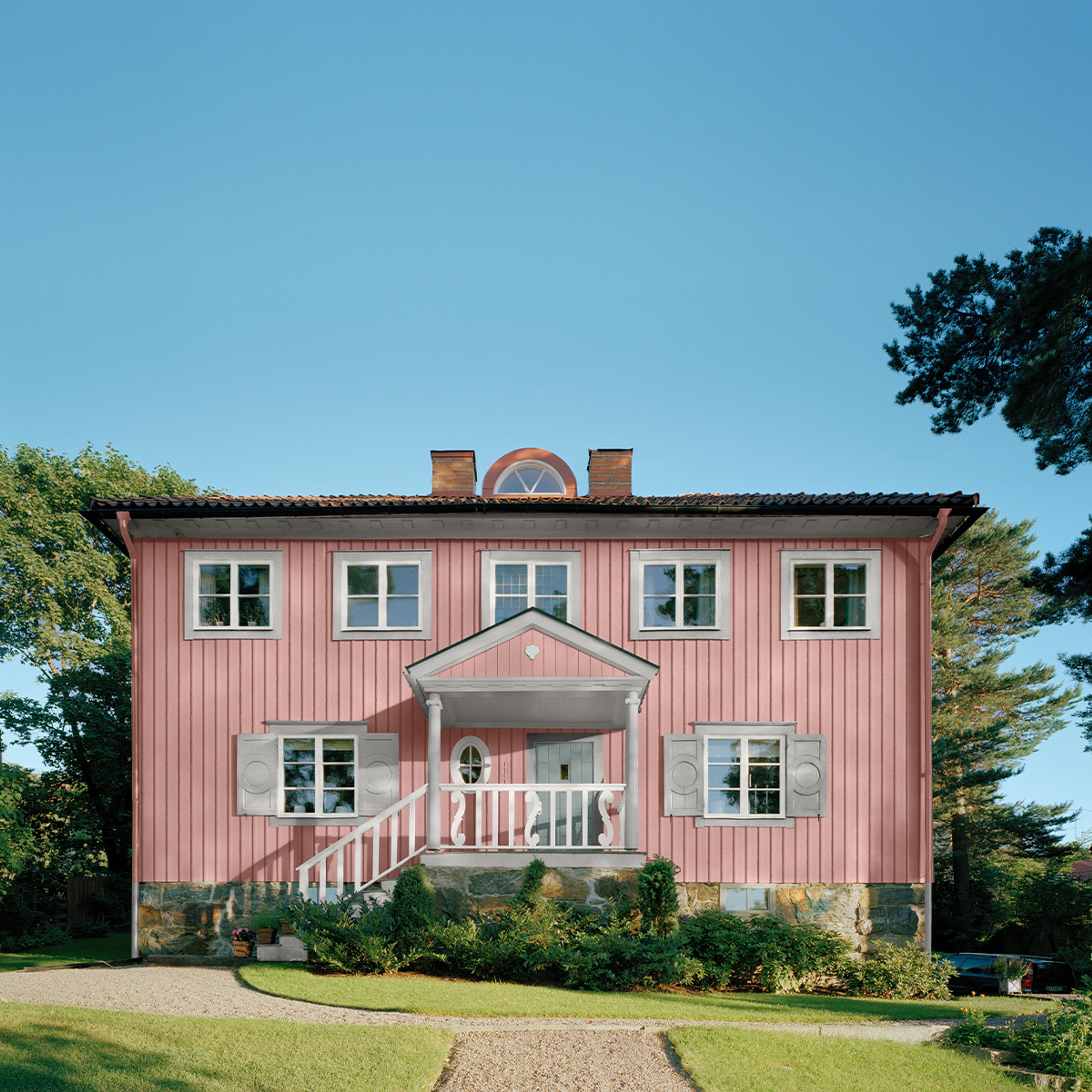 A two-story pink wooden house with white trim, grey shutters, a front porch, and a stone foundation.