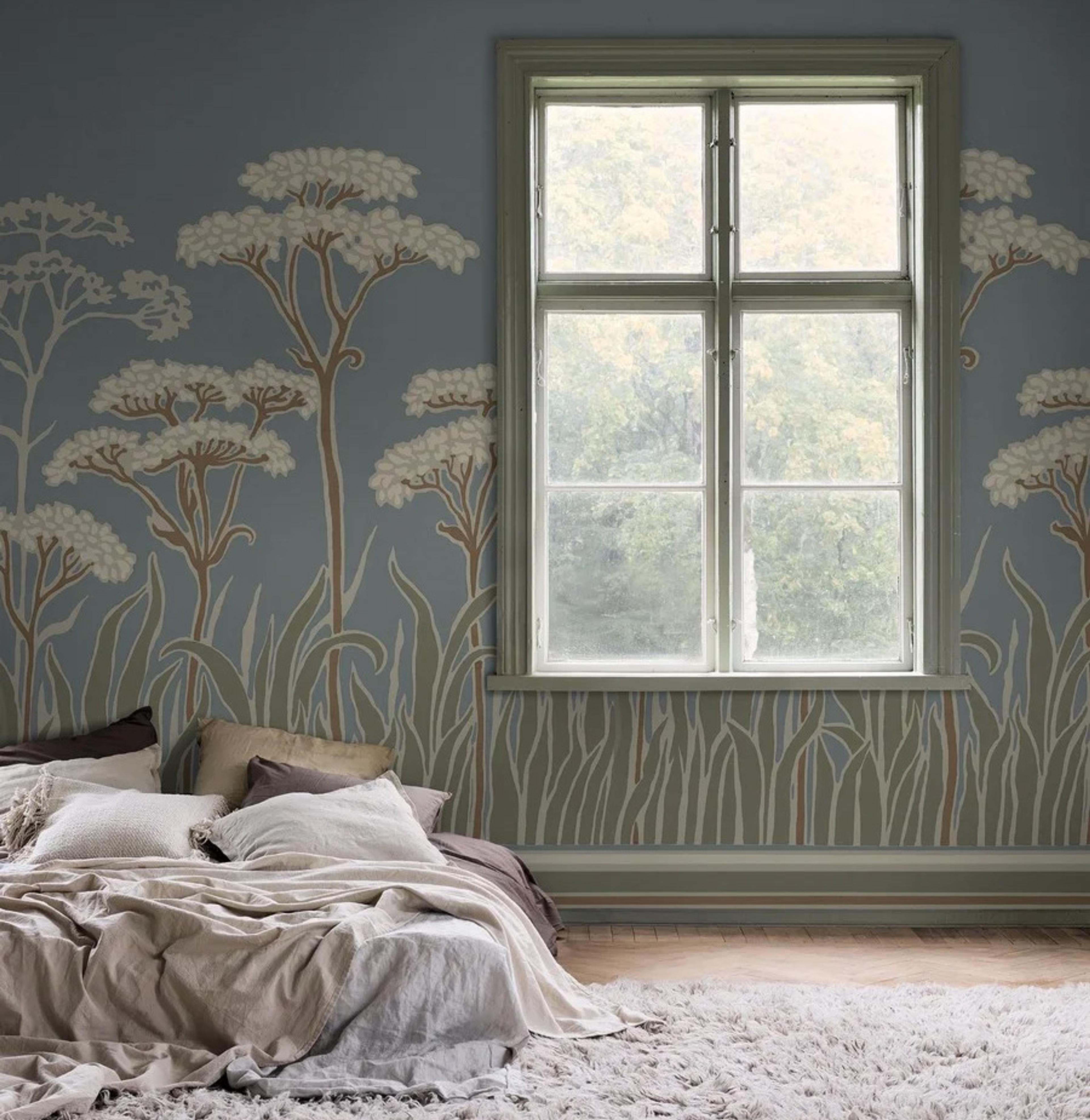 A serene bedroom with light blue botanical wallpaper, a large window, a bed with neutral linens, and a fluffy rug.