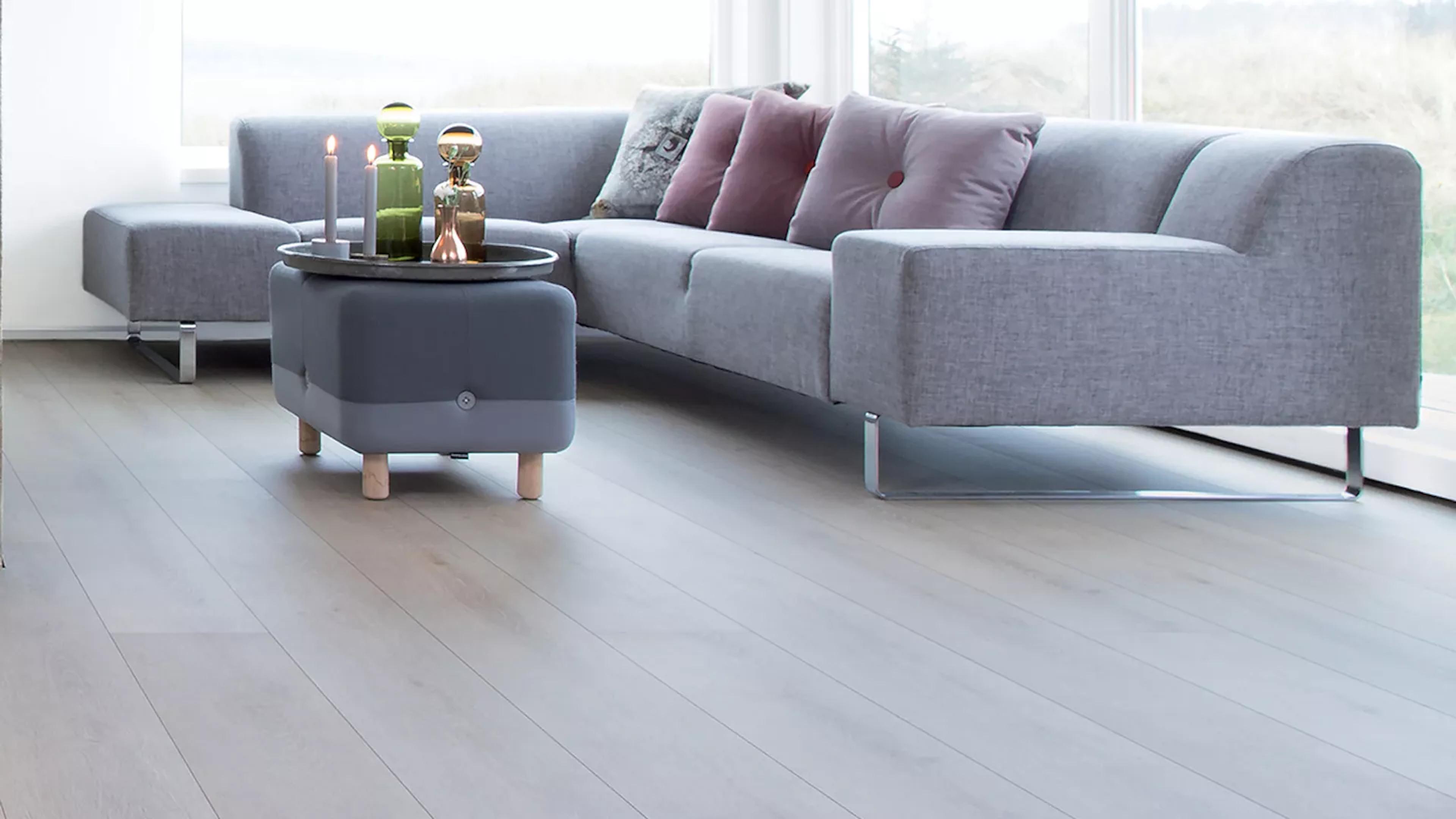 A modern living room featuring a grey sectional sofa, an ottoman, and light wood flooring.